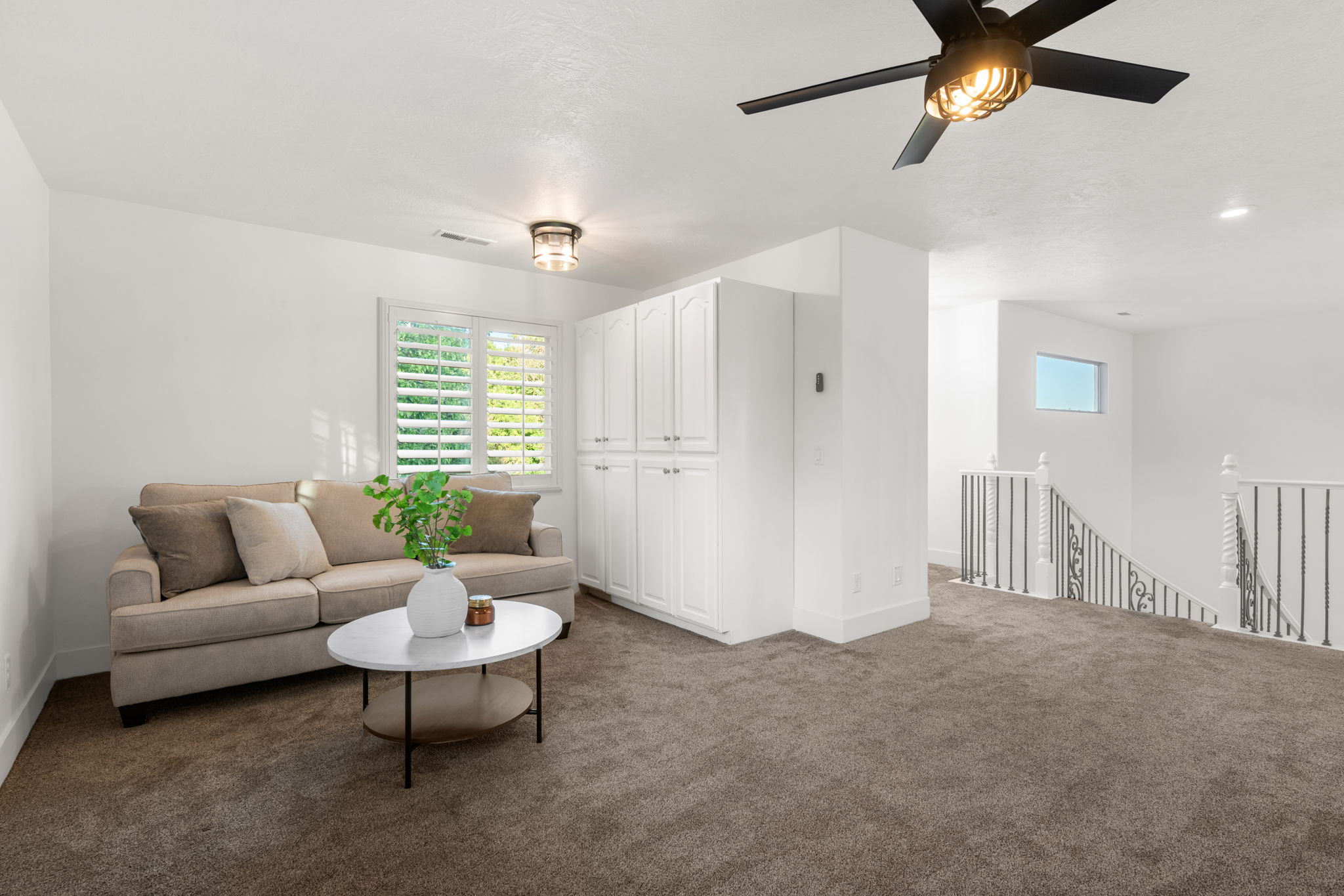 Carpeted loft area featuring a modern black ceiling fan, white built-in cabinetry, and white window shutters