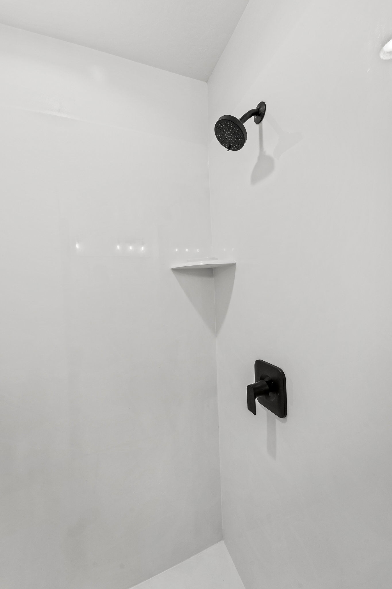 Shower enclosure featuring white paneling, a matte black showerhead, a built-in corner shelf, and a matte black single-handle control