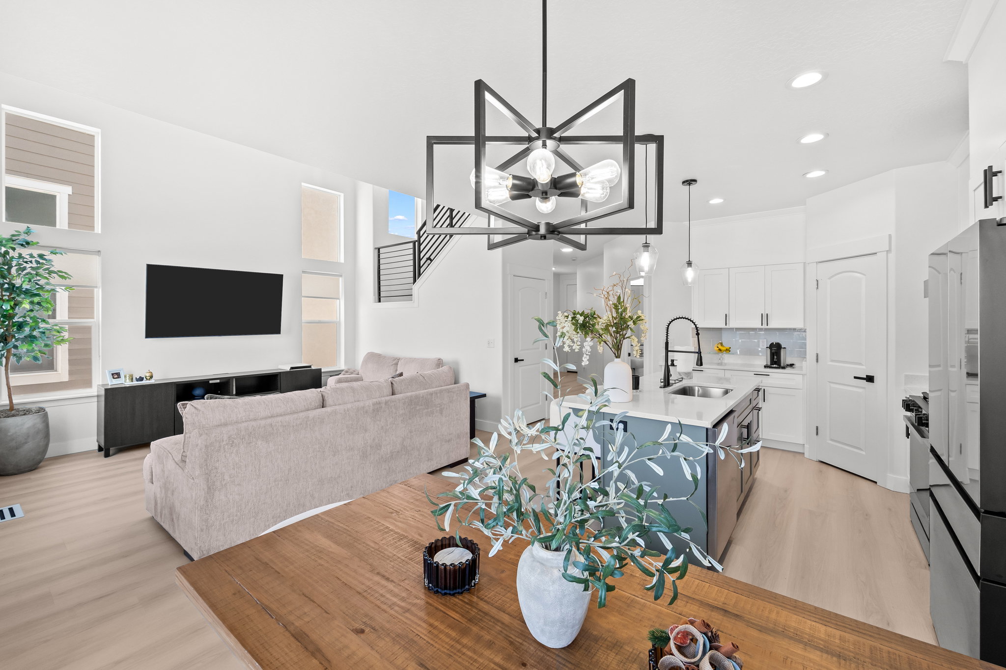Open-concept living space featuring high ceilings, wood-finish flooring, a modern chandelier, and a kitchen island with a sink and pendant lighting