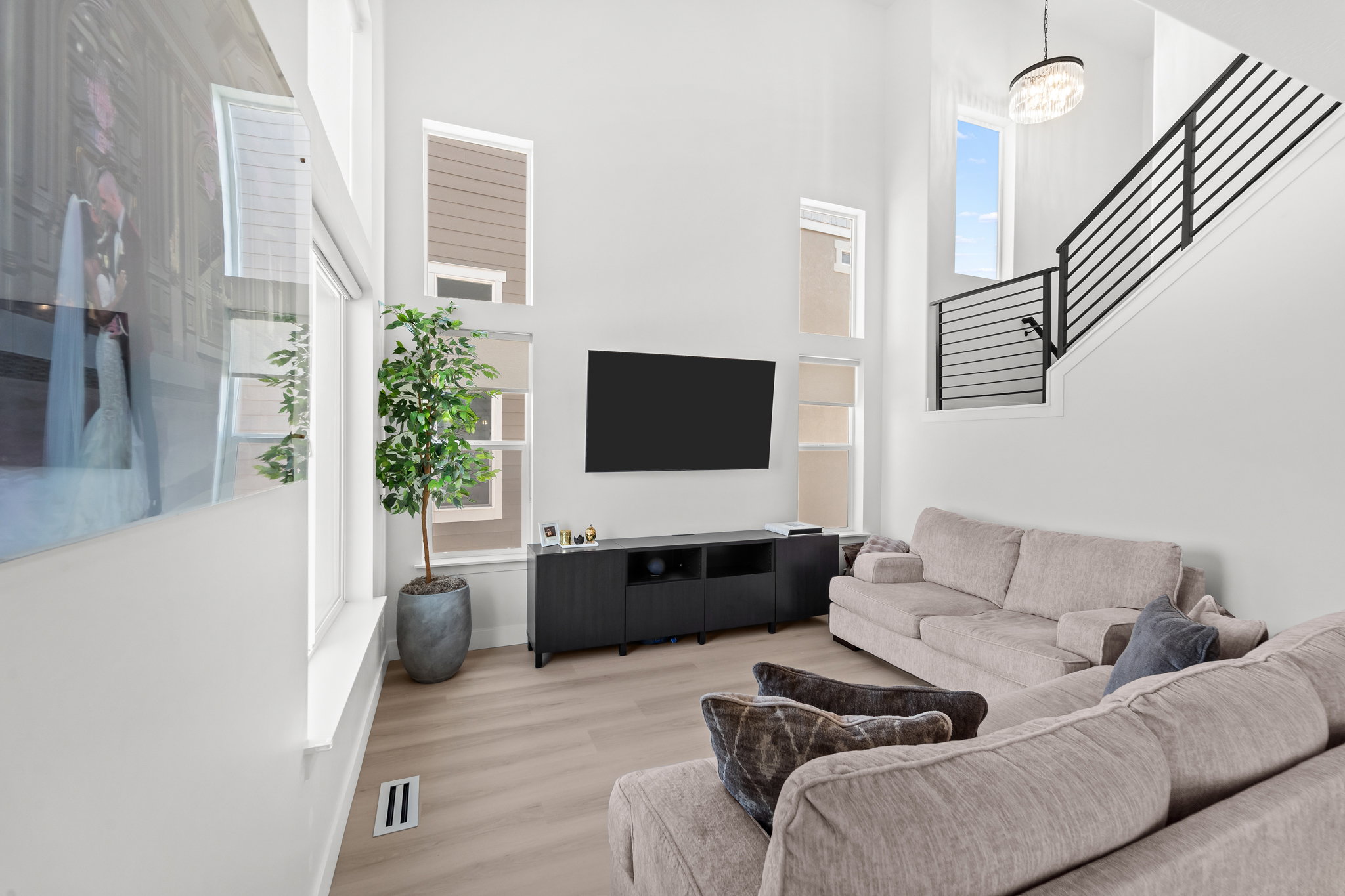 Vaulted living space featuring an open-riser staircase with black metal balusters, high ceilings, light wood-finish flooring, a wall-mounted media console, and a contemporary chandelier