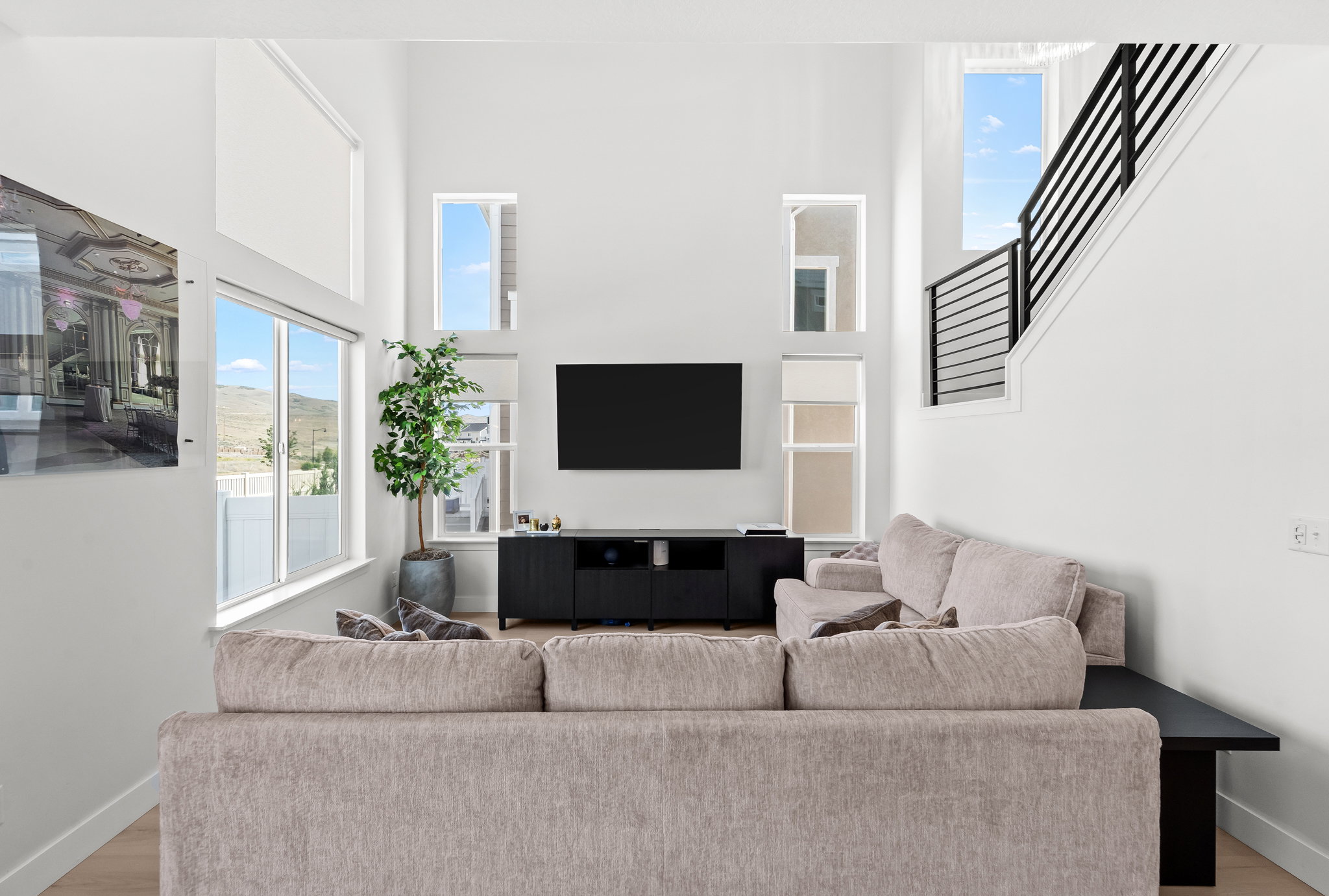 Two-story living area featuring tall ceilings, wood-finish flooring, a wall-mounted media console, and multiple windows