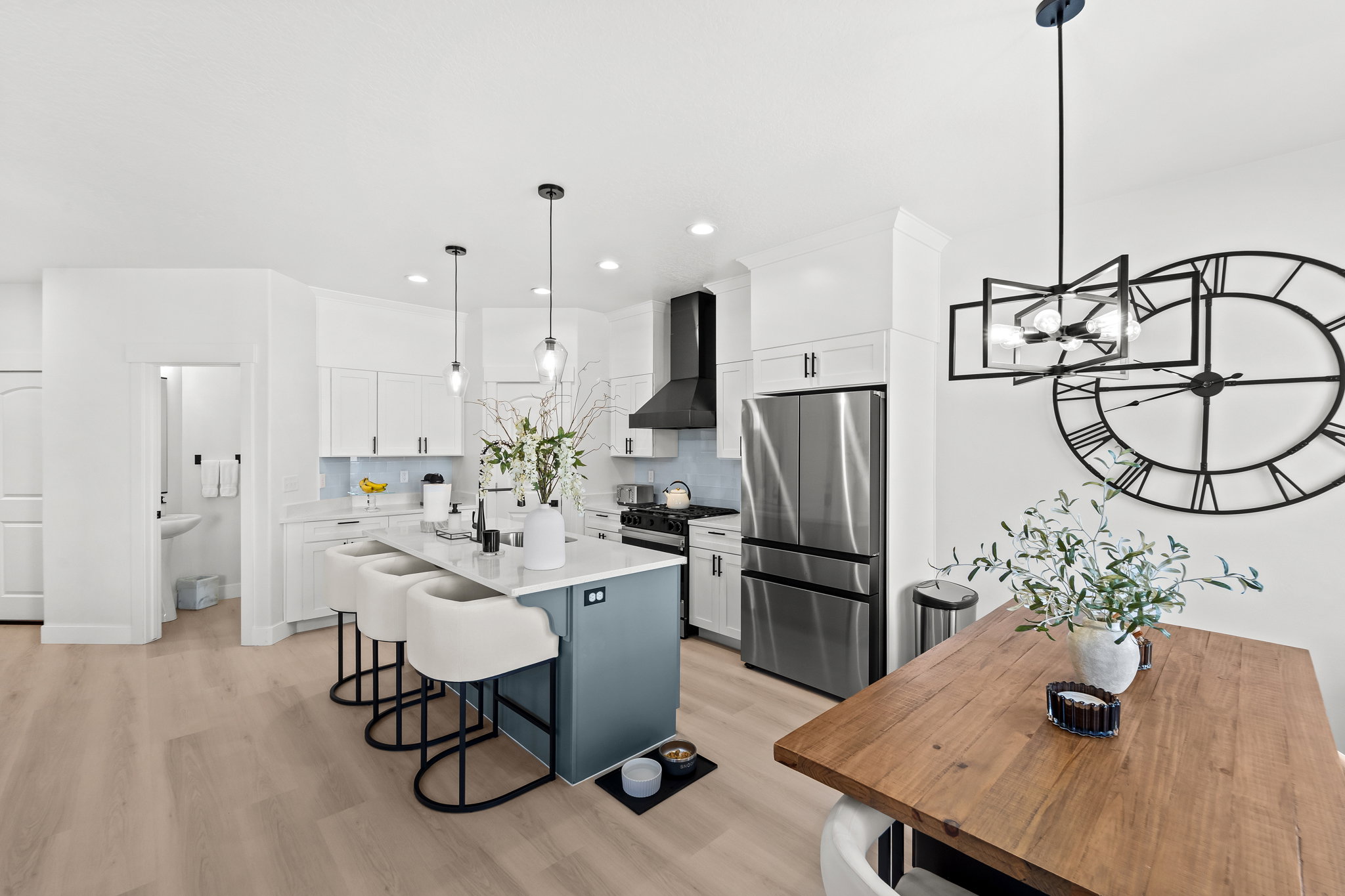 Open-concept kitchen featuring an oversized island with seating, pendant lighting, stainless steel appliances, white cabinetry, and wood-finish flooring