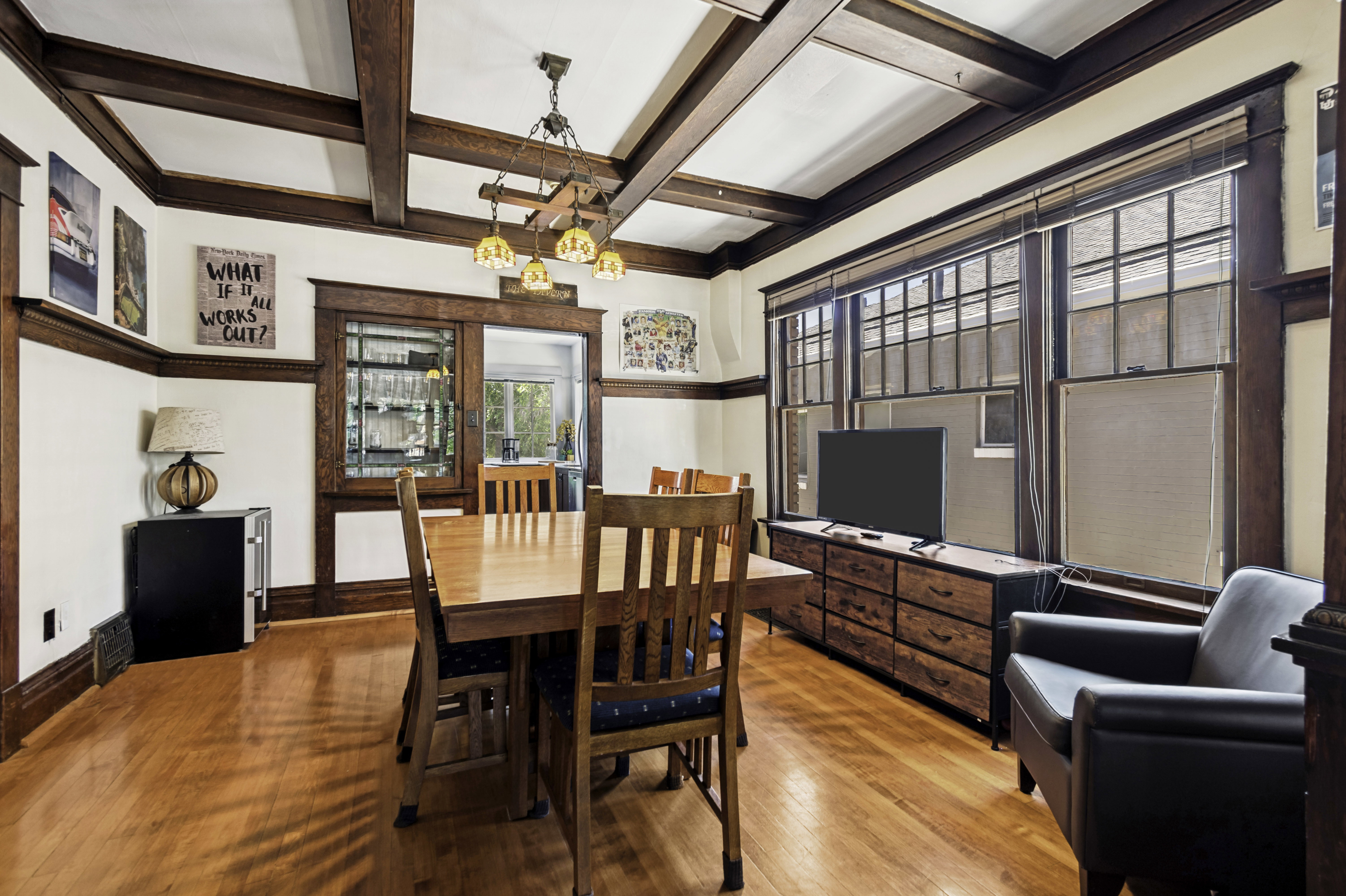 Hardwood flooring throughout, featuring a coffered ceiling with dark wood beams, extensive dark wood trim, and a built-in display cabinet with leaded glass panels