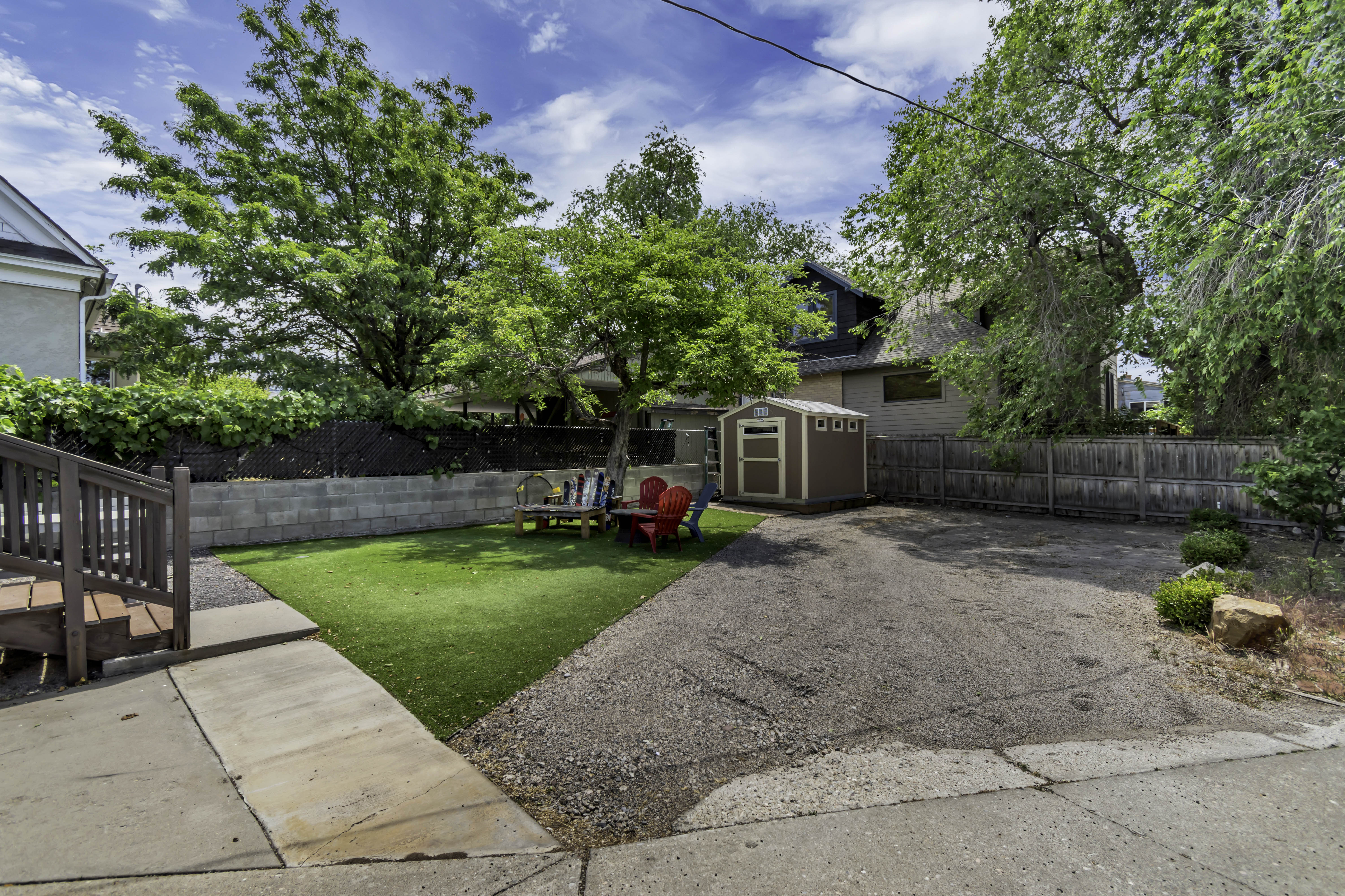 Expansive rear yard featuring a paved drive, artificial turf lawn, and mature trees
