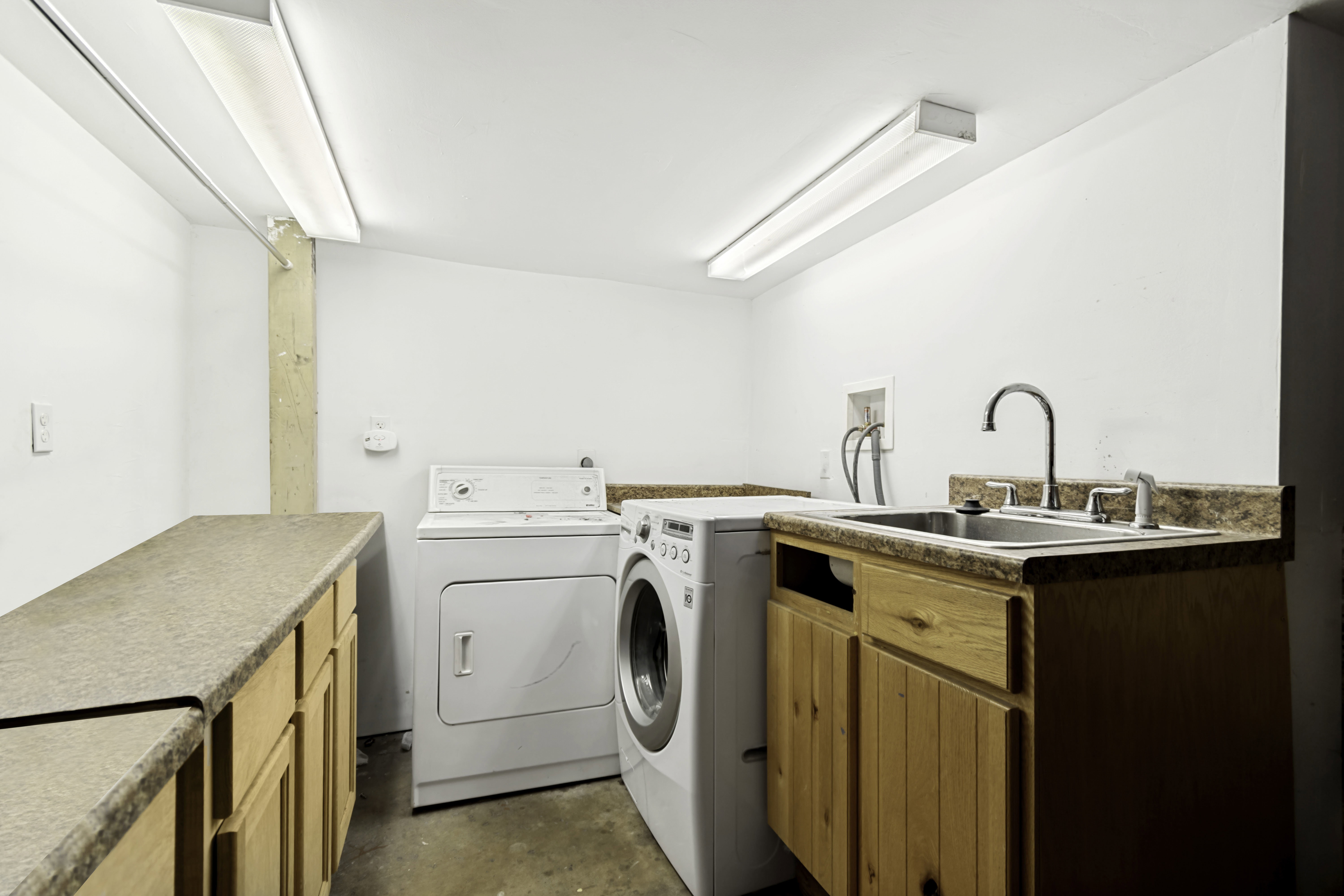Dedicated laundry area featuring a utility sink, wood-finish cabinetry, extensive countertop space, and overhead fluorescent lighting