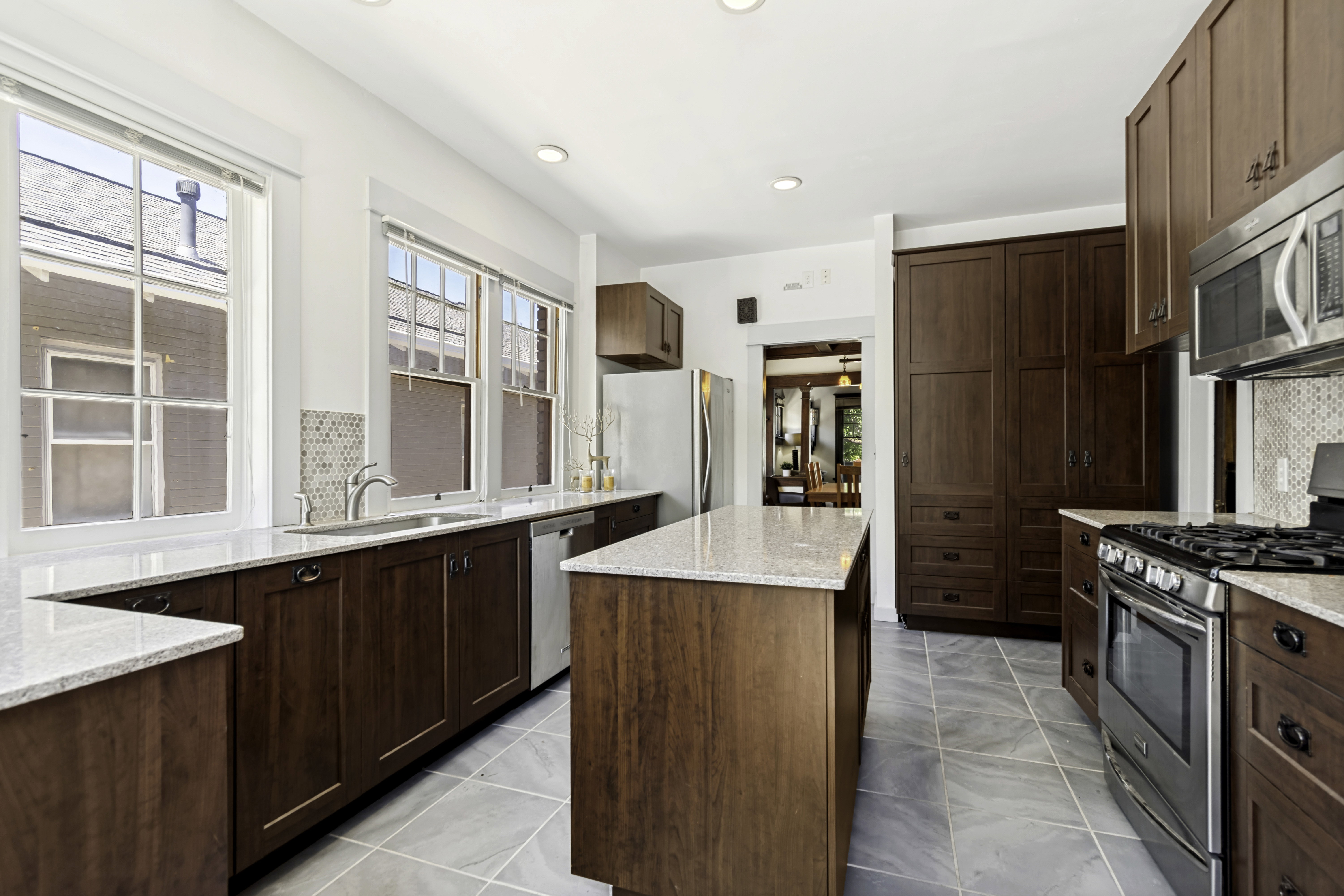 Kitchen featuring wood-finish cabinetry, light-toned countertops, a central island, stainless steel appliances, and a mosaic tile backsplash