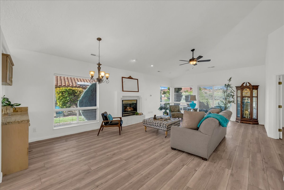 Expansive living area featuring wood-finish flooring, a white-painted fireplace with a hearth, vaulted ceilings, and a ceiling fan