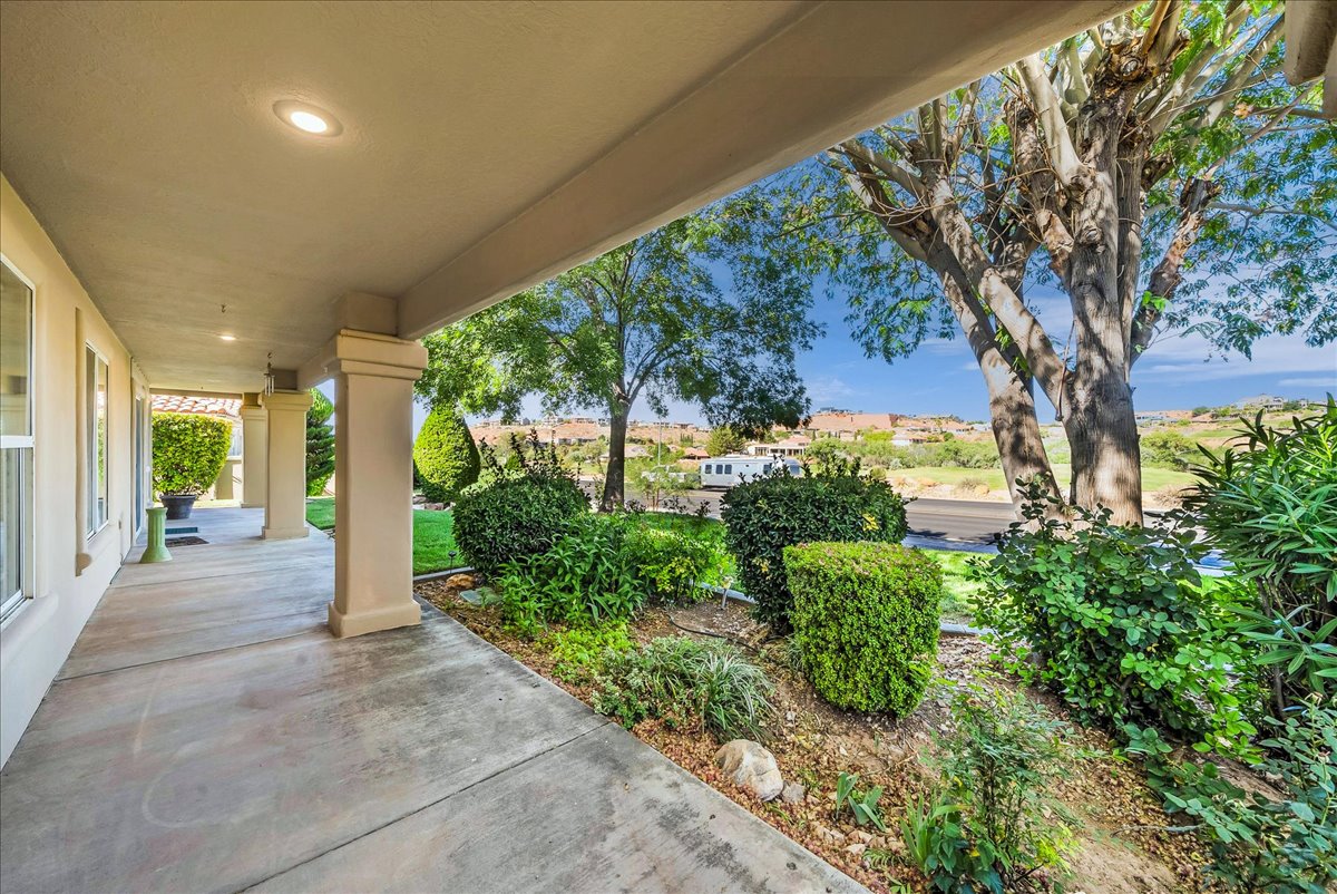 Covered concrete patio with recessed lighting, supported by square columns, overlooking a landscaped garden bed with mature trees and established shrubs
