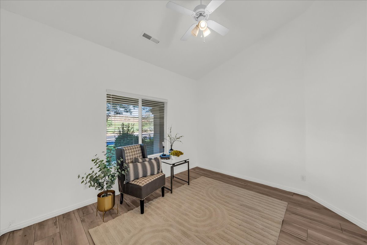 Room featuring wood-finish flooring, a white ceiling fan with integrated lighting, and a large window with blinds