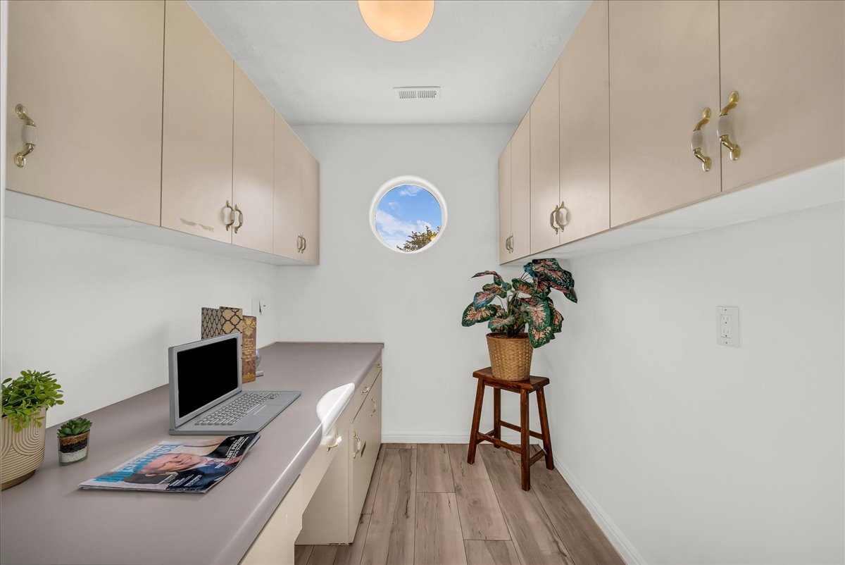 Dedicated workspace featuring a circular window, extensive overhead cabinetry with decorative hardware, a built-in desk, wood-finish flooring, and white walls