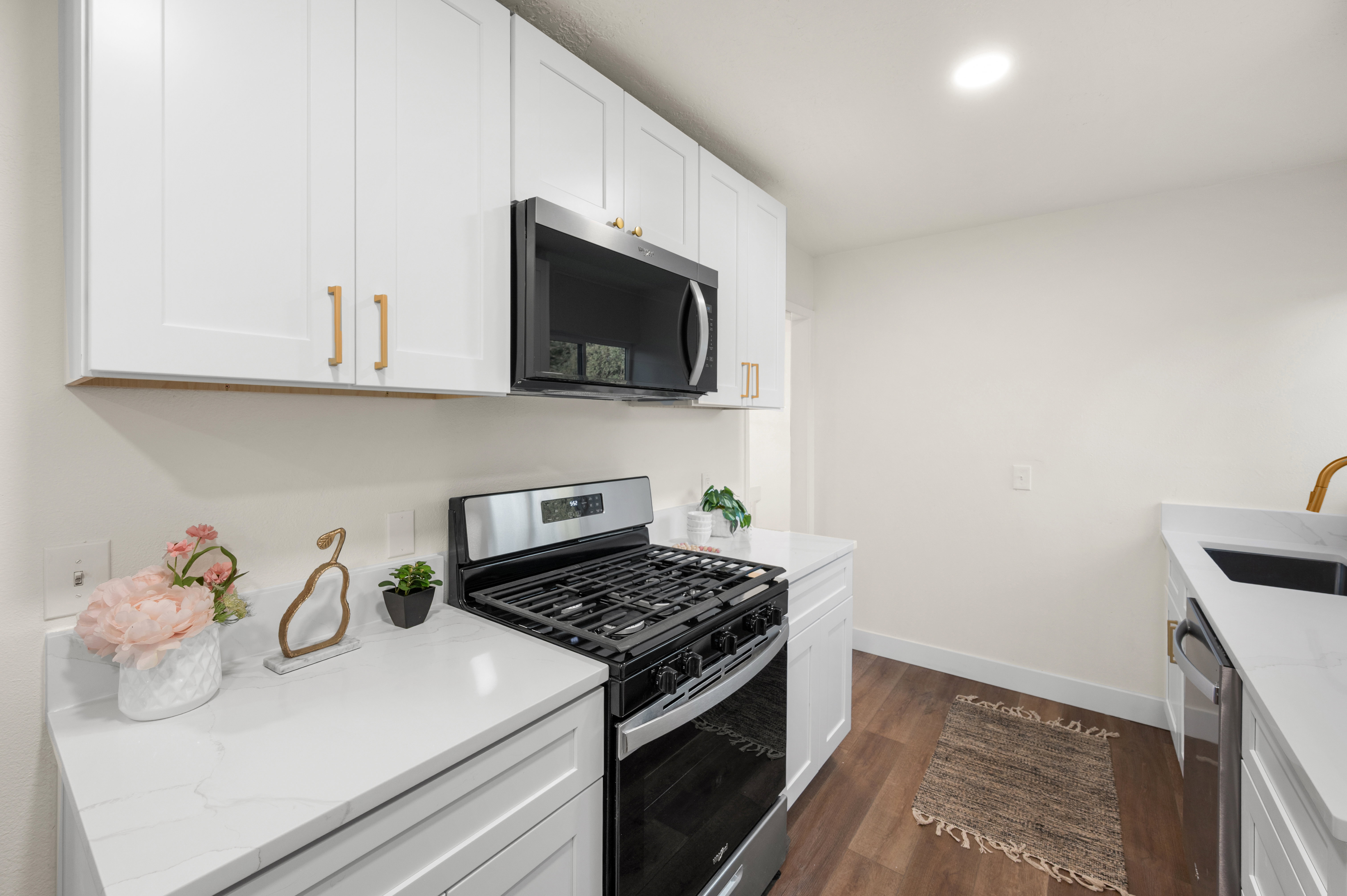 Kitchen featuring white shaker cabinetry, stainless steel range with gas burners, built-in microwave, white stone countertops, and wood-finish flooring
