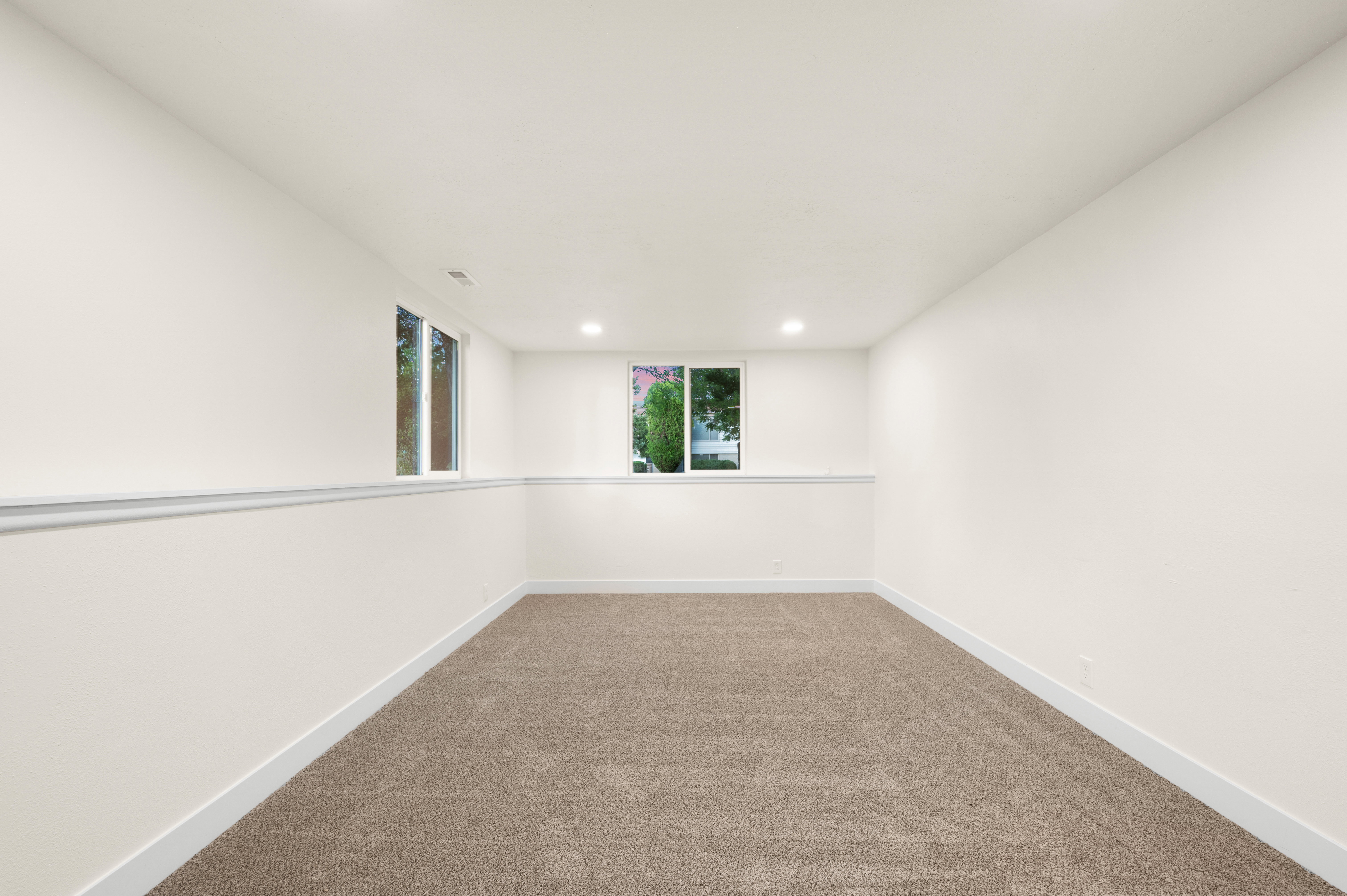 Spacious room featuring neutral carpeting, white painted walls, white trim, recessed lighting, and dual windows