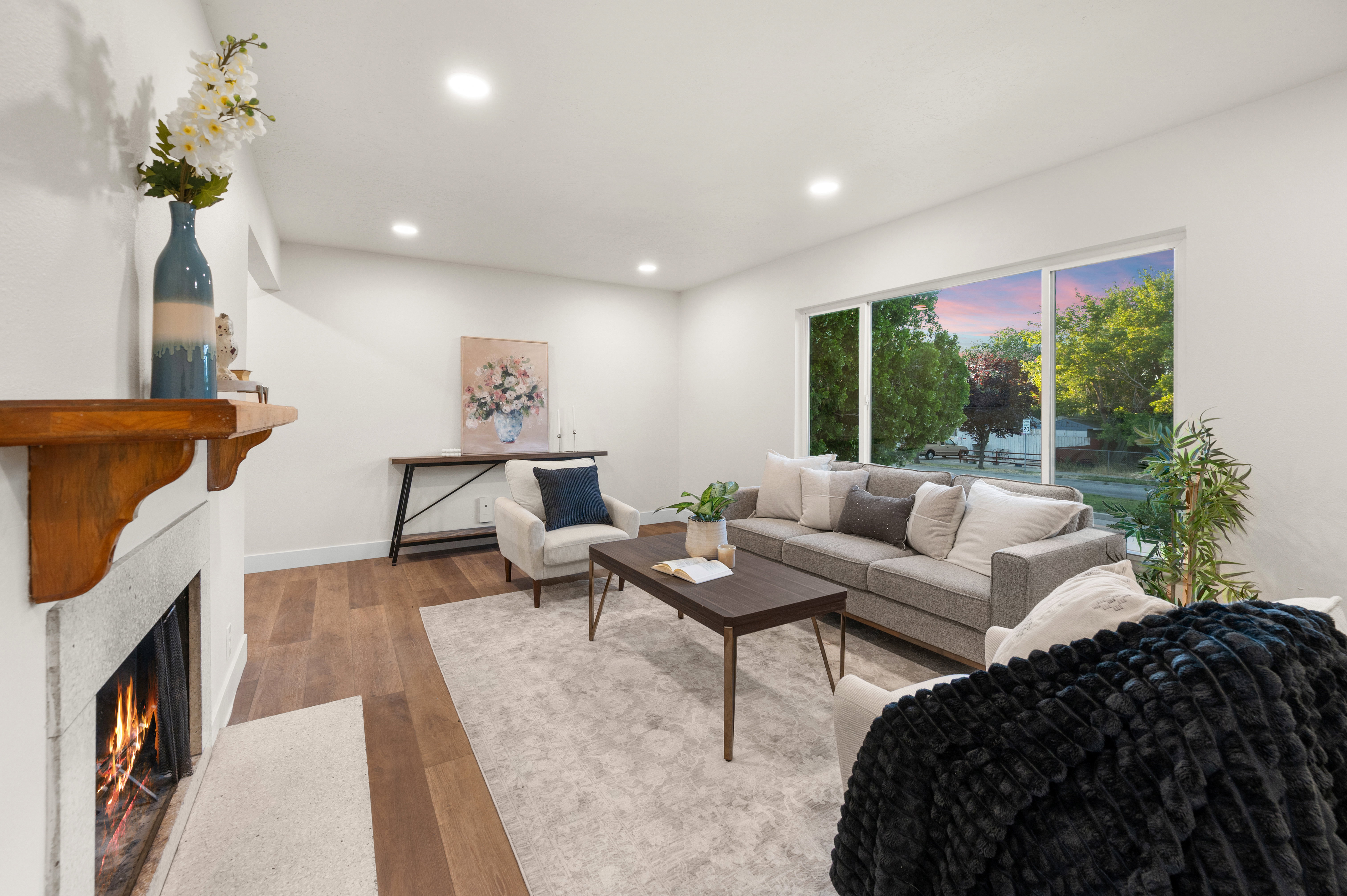 Living area featuring wood-finish flooring, a stone fireplace with a wood mantle, a large picture window, and recessed lighting