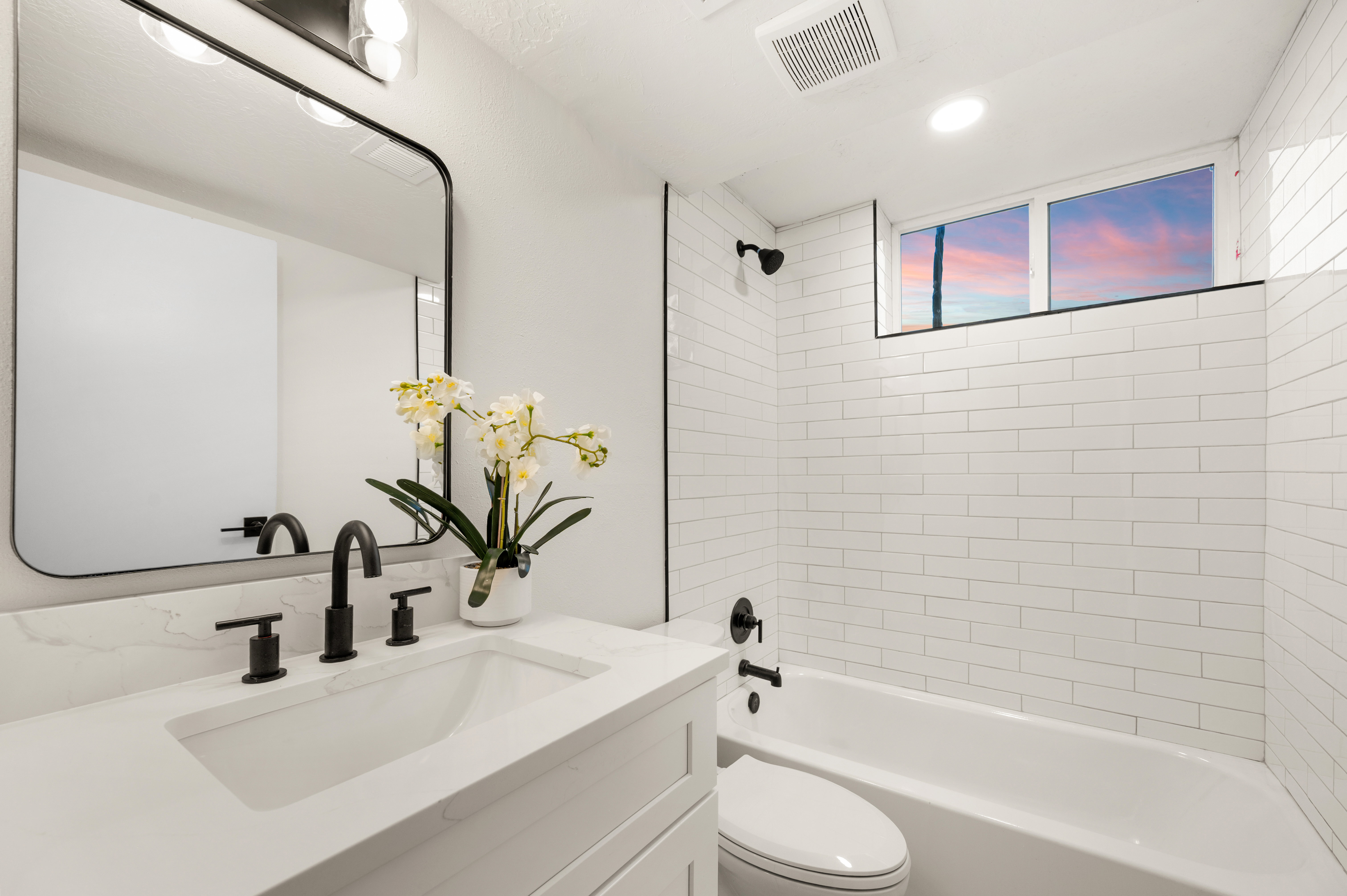 Bathroom featuring a white subway tile shower surround, matte black fixtures, an elongated white vanity with an integrated sink, a large framed mirror, and recessed lighting
