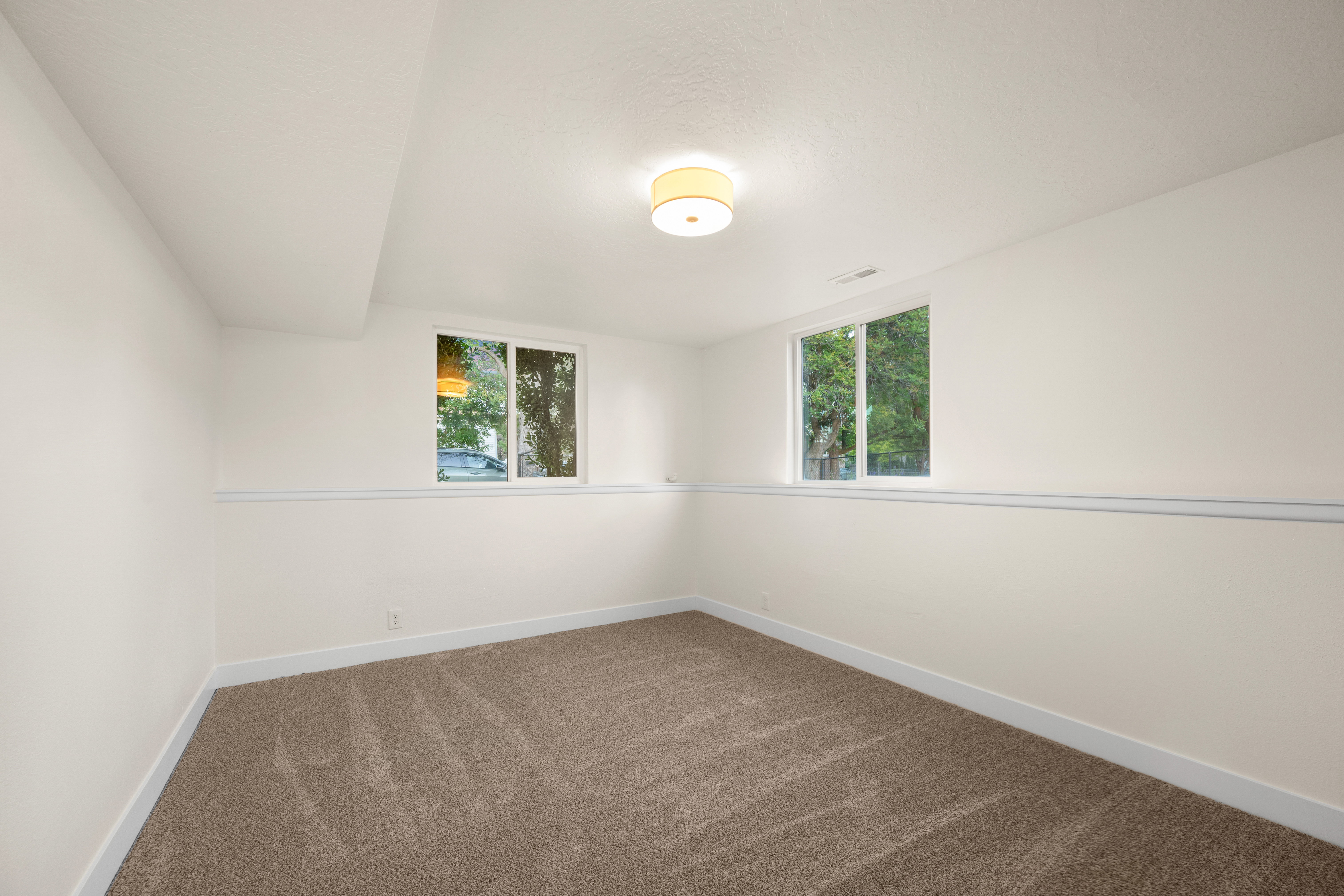 Finished room featuring neutral carpeting, white walls with chair rail molding, and two windows providing natural light