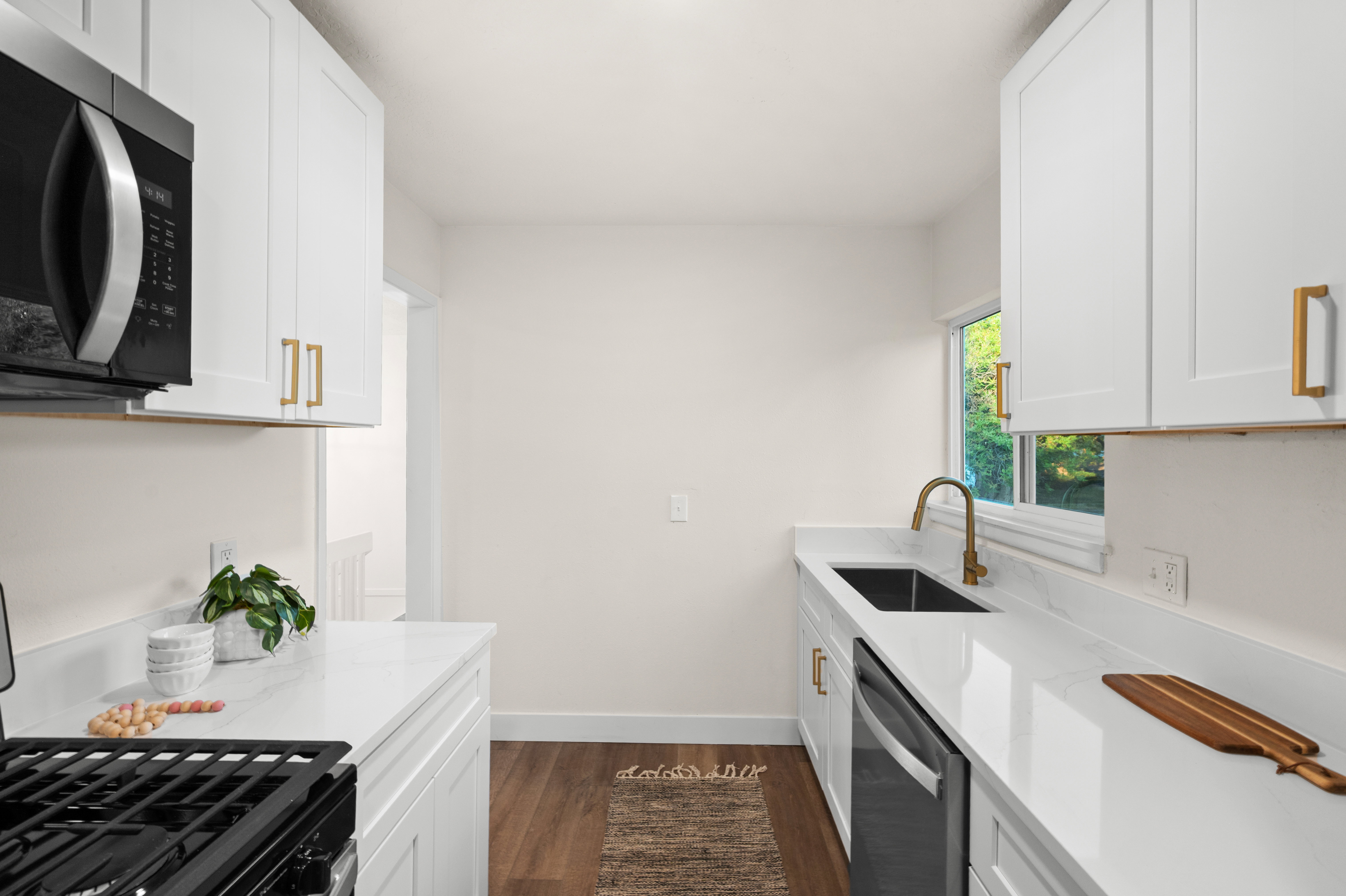 Modern kitchen featuring white shaker cabinetry with gold-tone hardware, white countertops, wood-finish flooring, a black gas range, and an undermount sink with a brass faucet