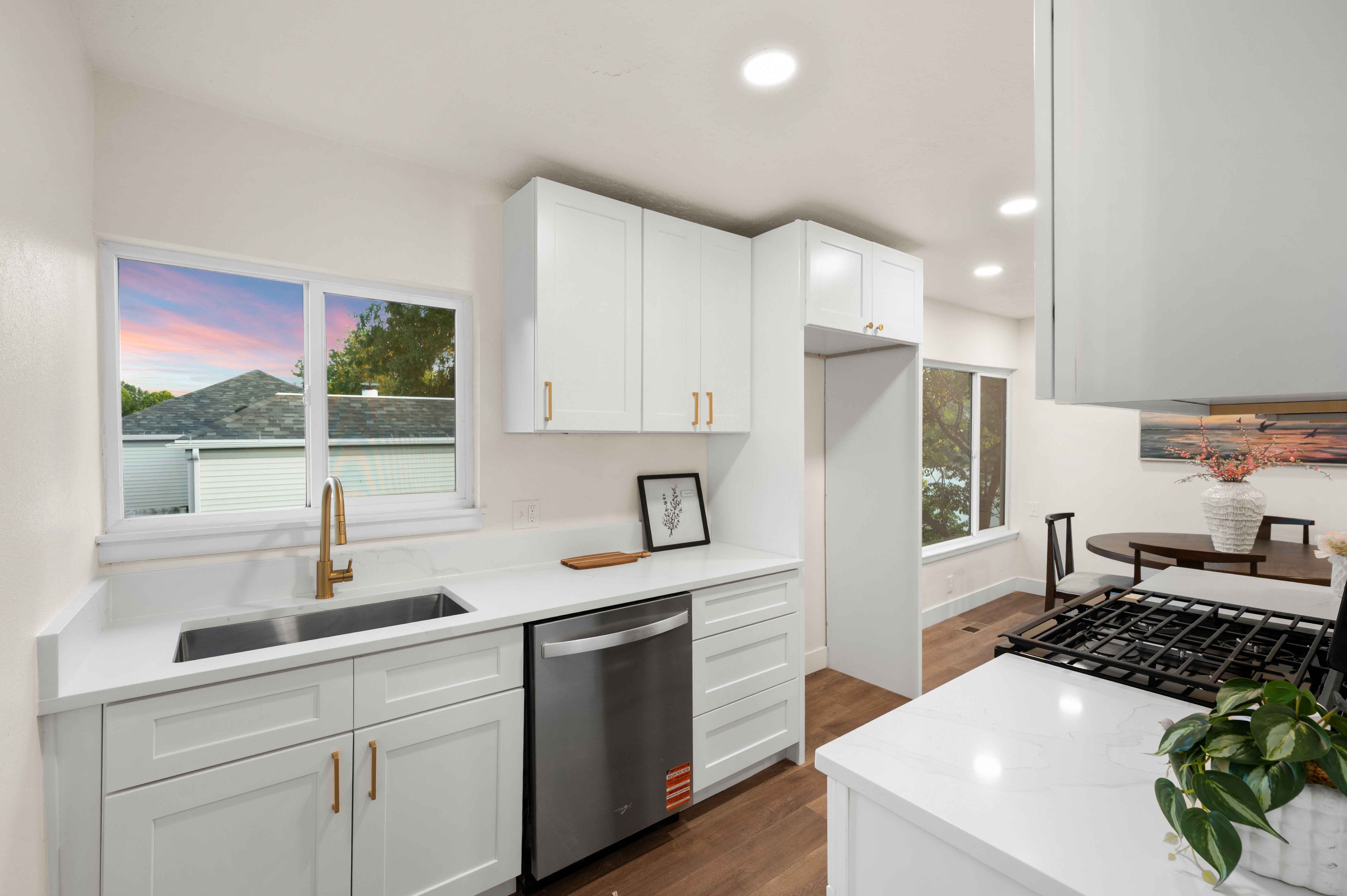 Kitchen featuring white shaker cabinetry, stainless steel dishwasher, undermount sink with a brass-finish faucet, white countertops, and wood-finish flooring