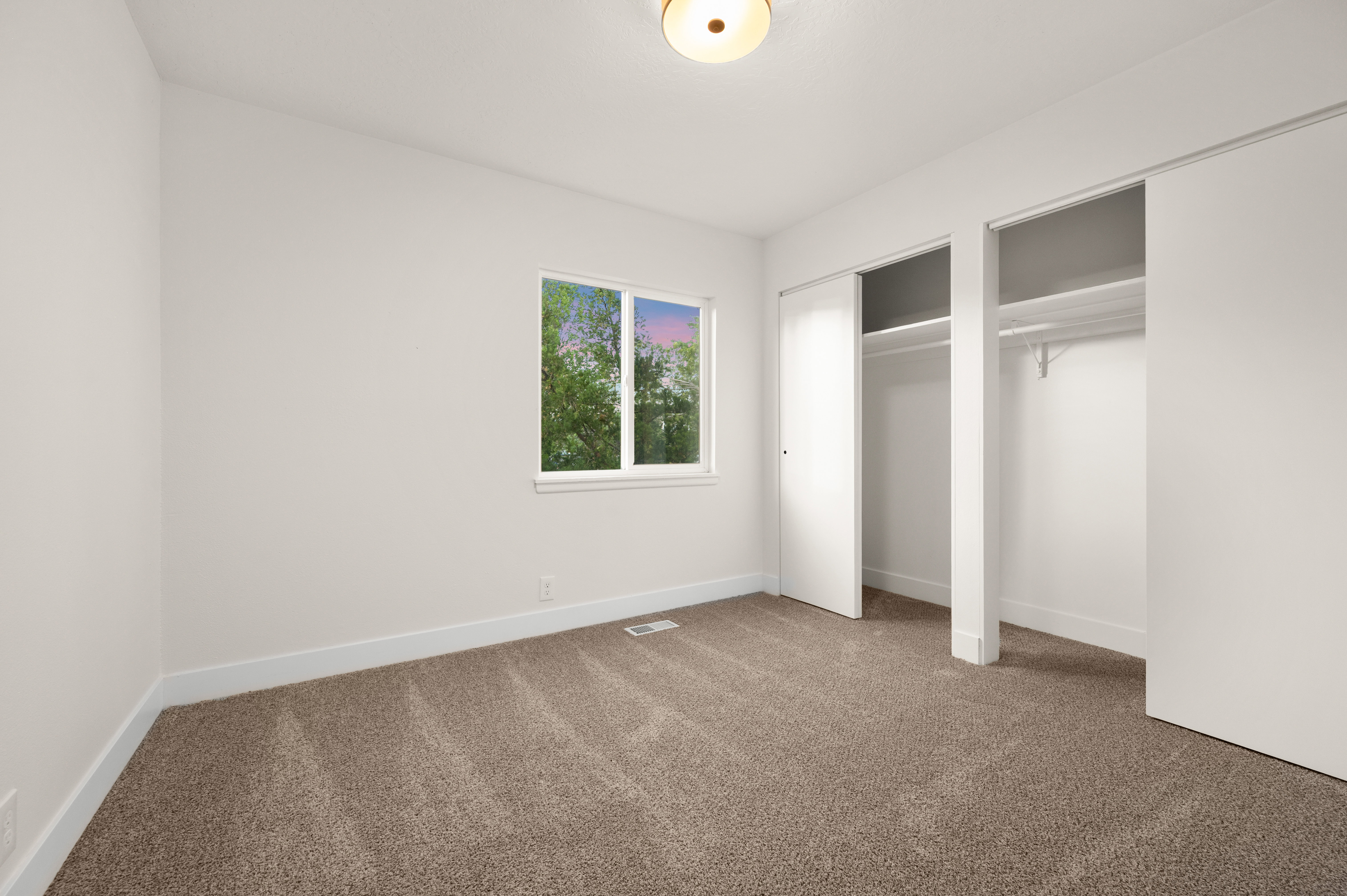 Bedroom featuring plush carpet flooring, a large window, ample natural light, two built-in closets with shelving, and a ceiling-mounted light fixture
