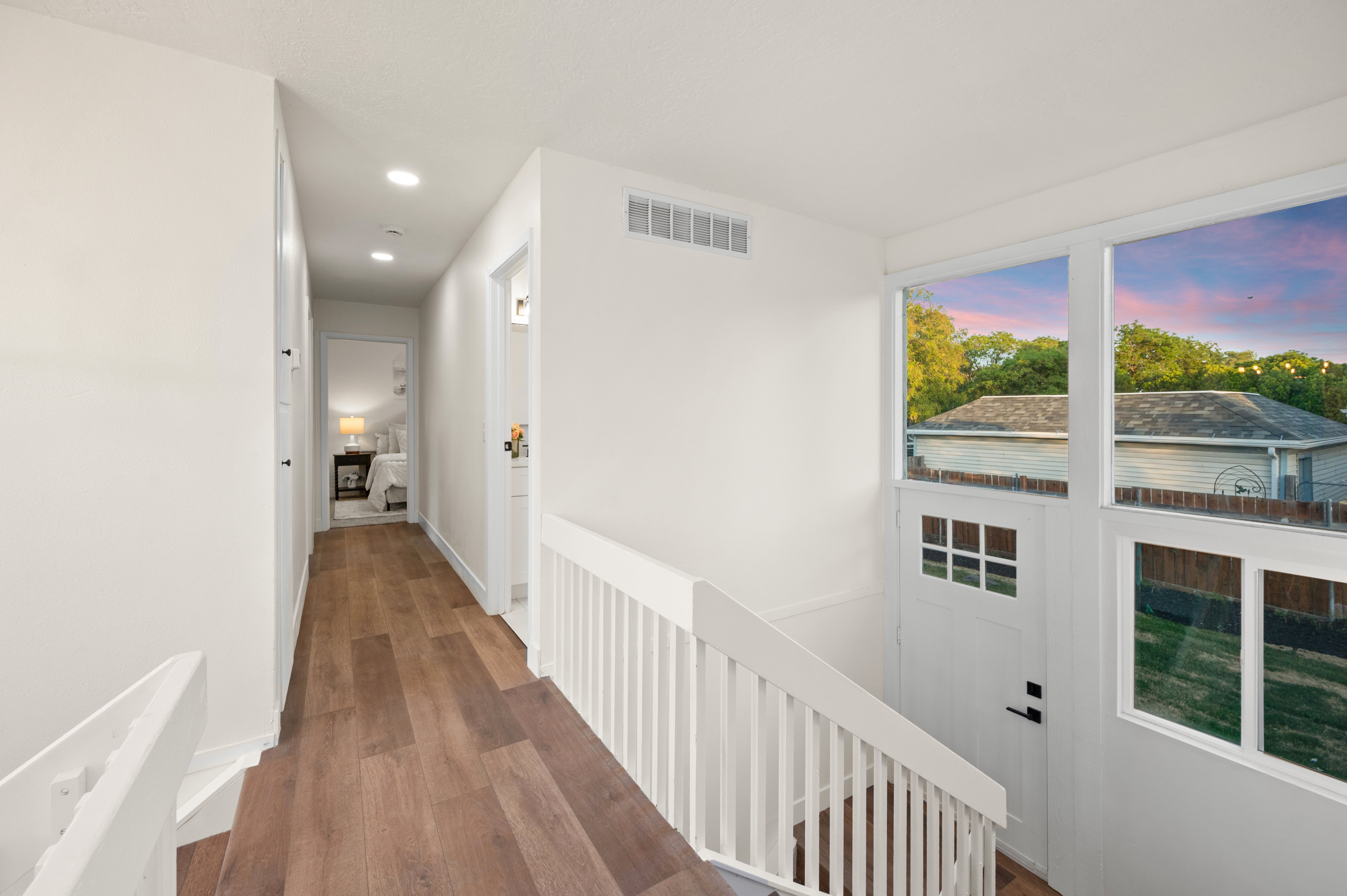 Upper-level landing featuring wood-finish flooring, recessed lighting, and a white staircase with spindle railing