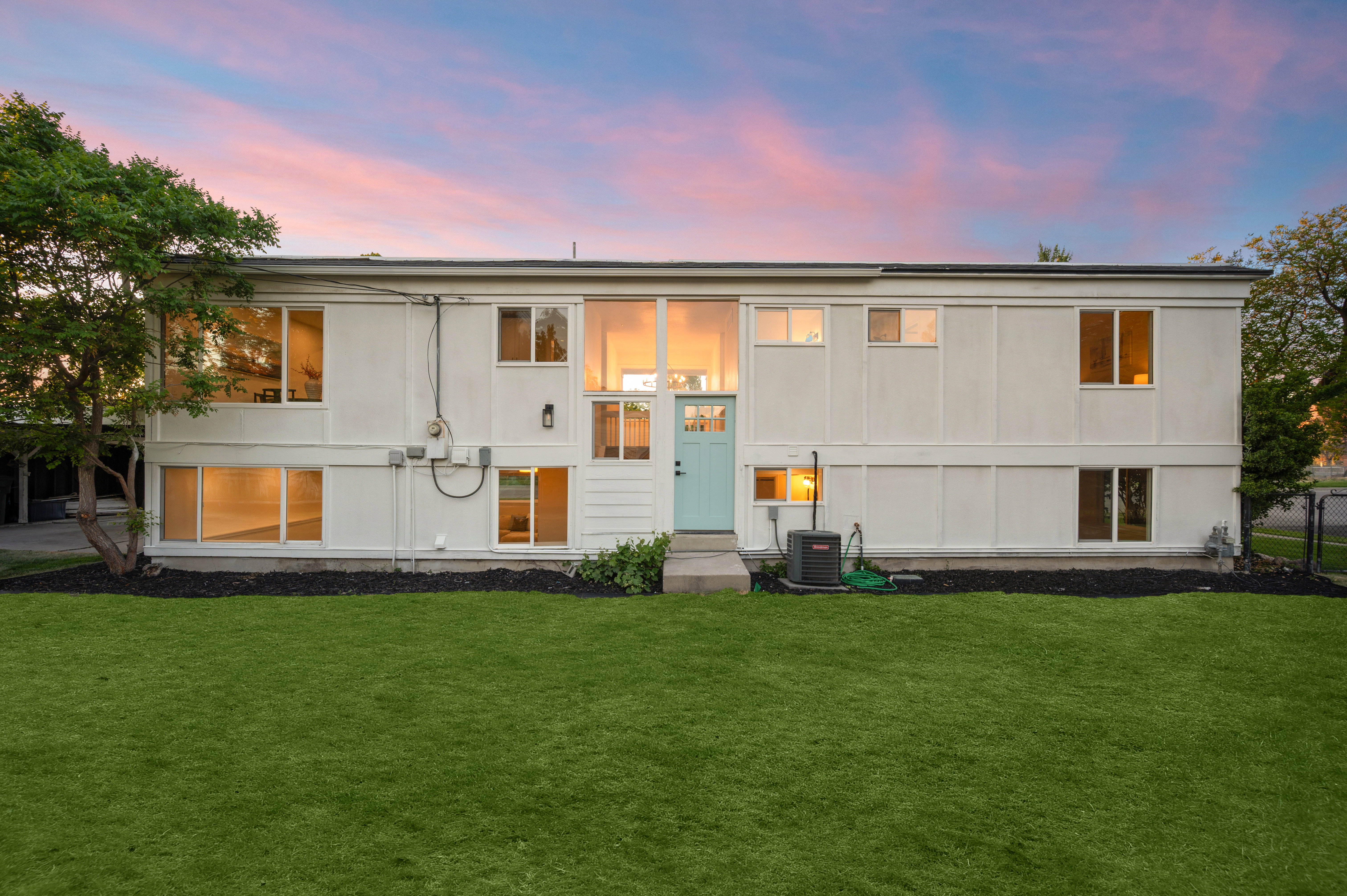 Modernist exterior featuring multiple large windows, a two-story entrance with transom windows, a light blue front door, and a manicured lawn