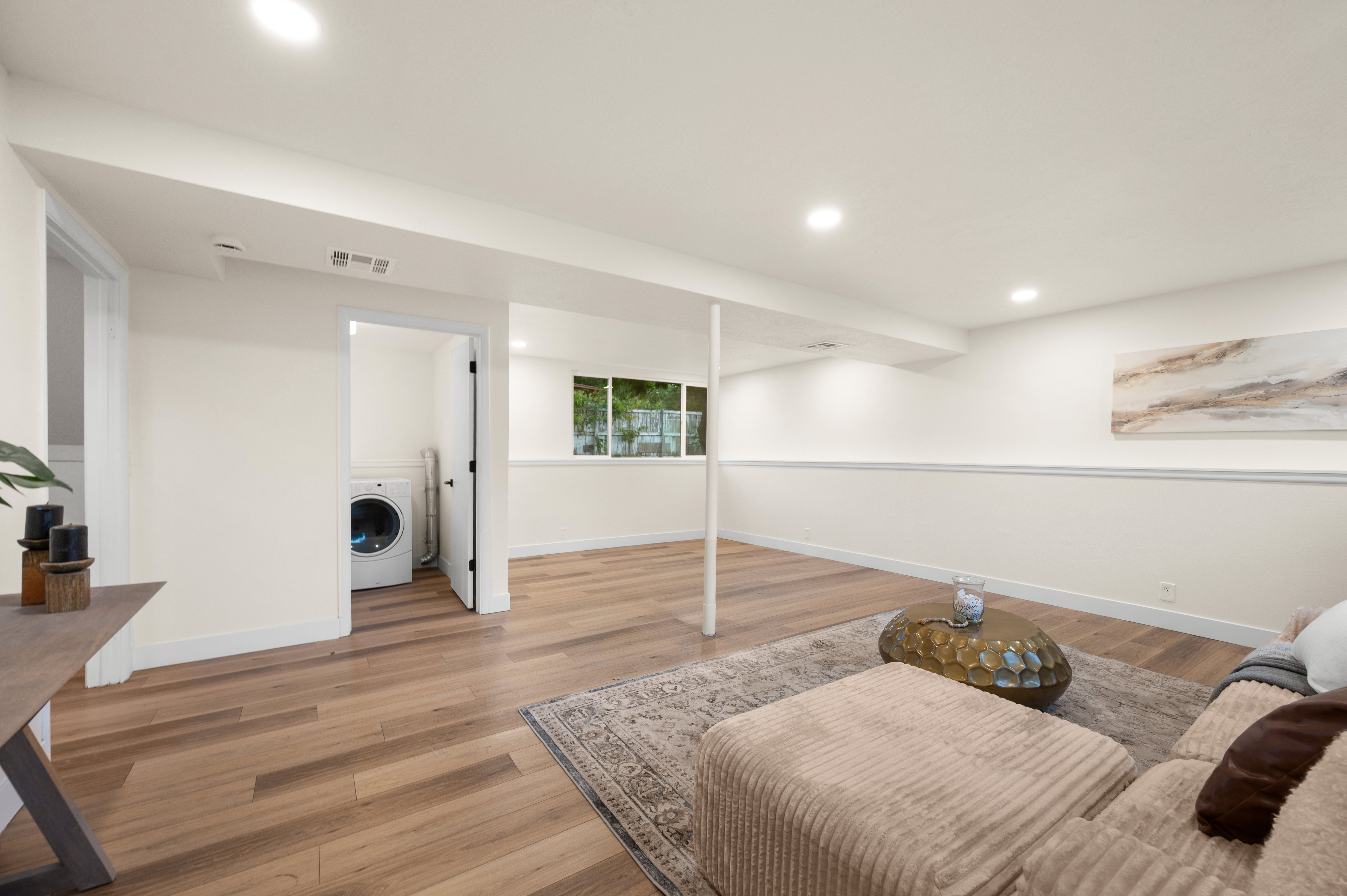 Spacious lower-level area featuring wood-finish flooring, recessed lighting, and a dedicated laundry alcove with a visible washer
