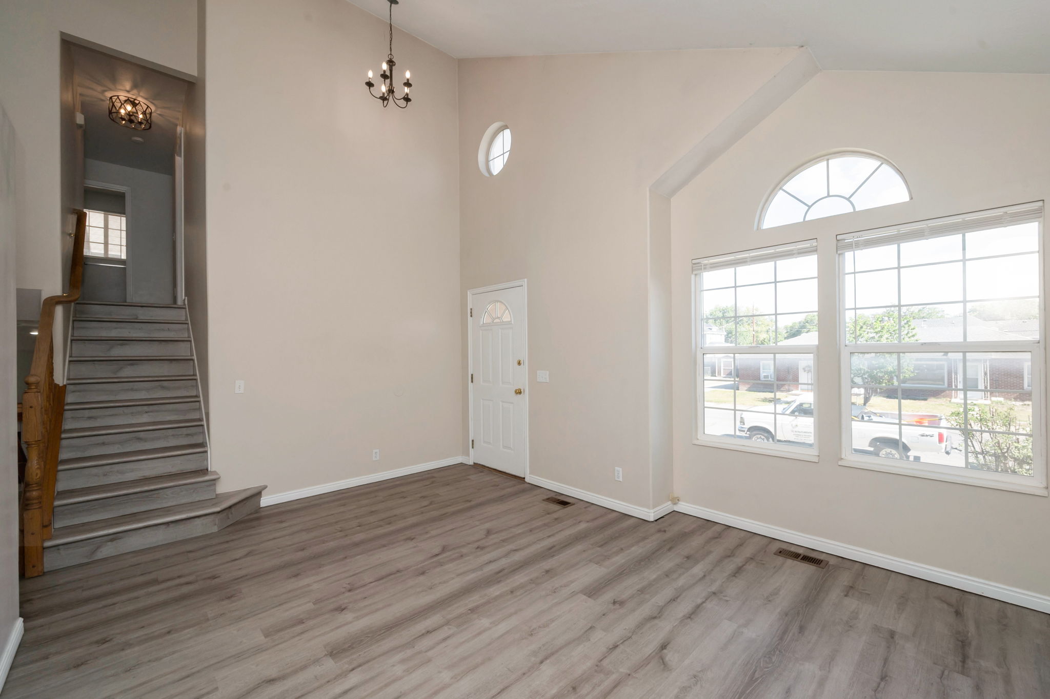Vaulted living area featuring wood-finish flooring, a decorative chandelier, and an arched window with a transom
