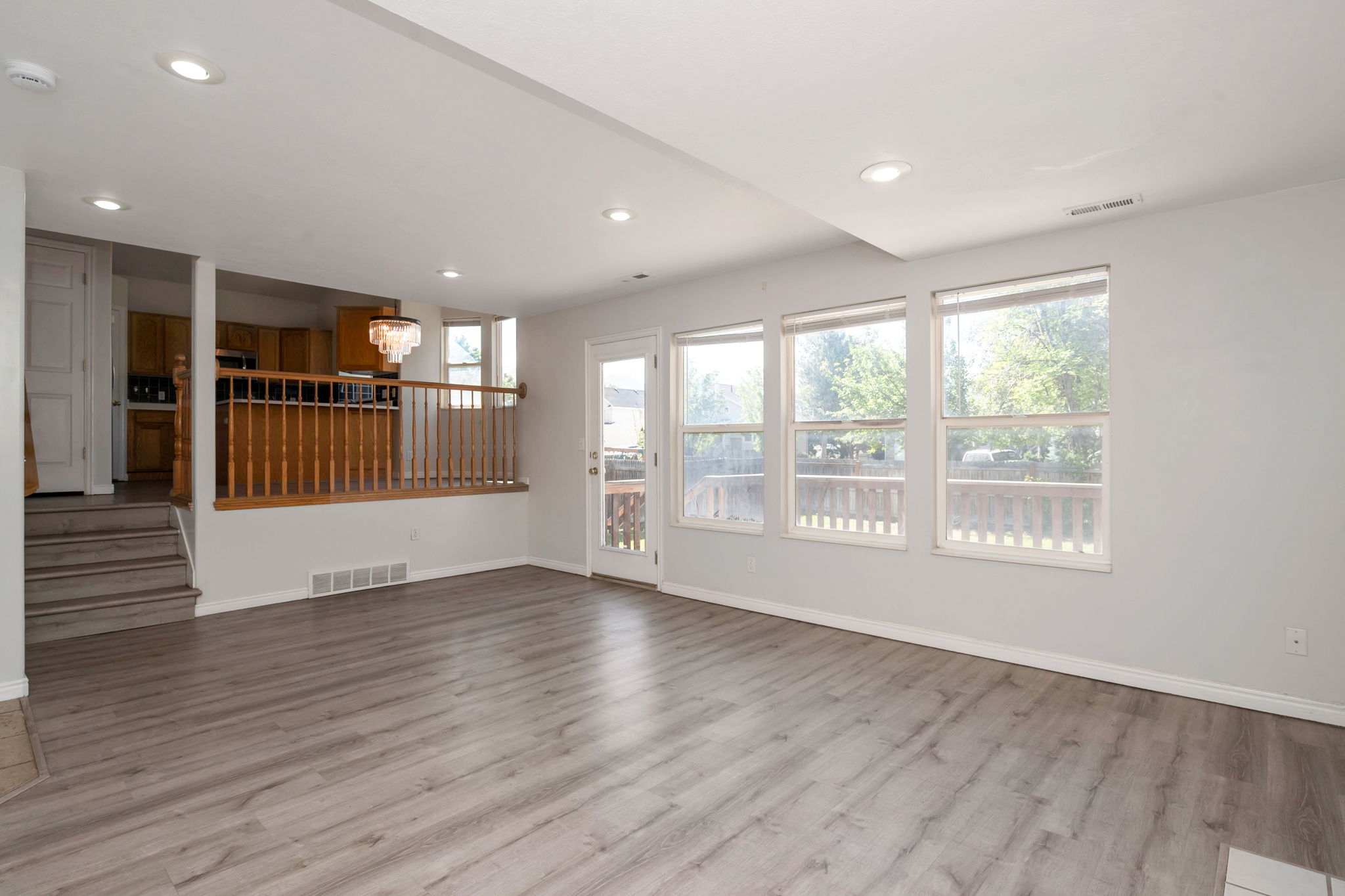 Spacious living area featuring light wood-finish flooring, recessed lighting, and a series of three large windows providing abundant natural illumination
