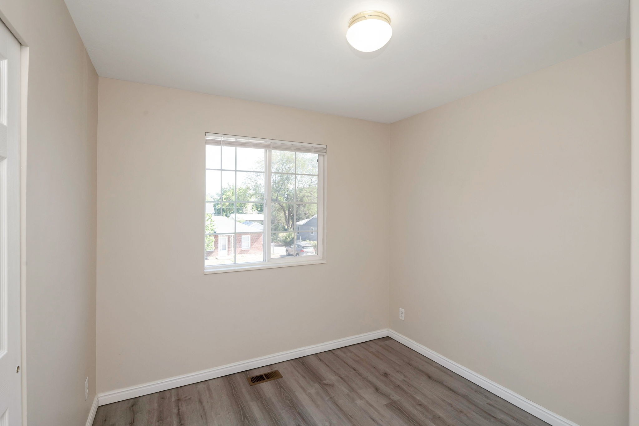 Neutral tone painted walls, wood-finish flooring, white window frame with horizontal blinds, white baseboards, and a flush-mount ceiling light fixture