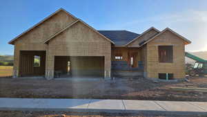 Newly framed residential structure featuring a dark shingled roof, multiple gables, and an attached two-car garage
