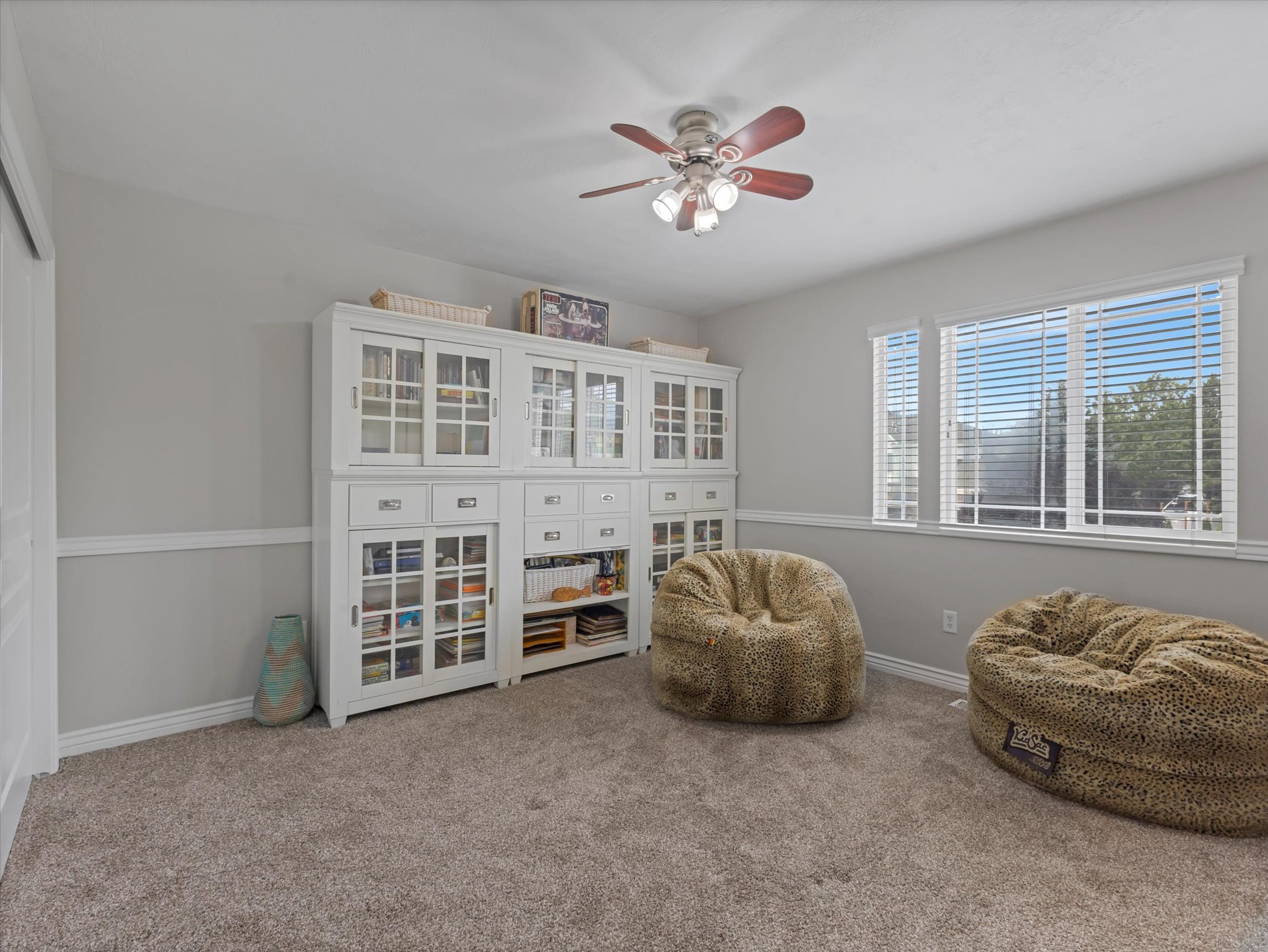 Secondary bedroom featuring light gray walls with chair rail molding, two windows with white blinds, a ceiling fan with light fixture, and neutral carpet flooring