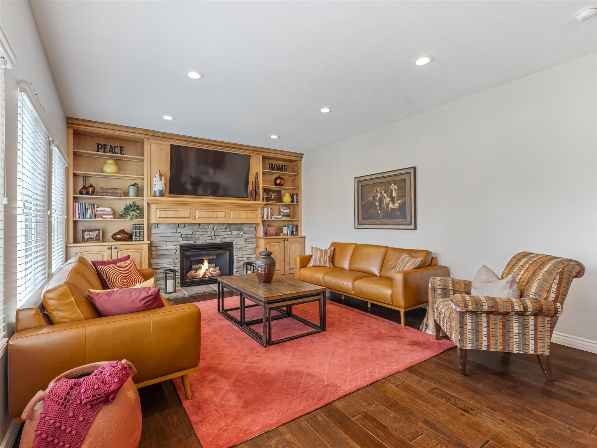 Living area featuring a stone-clad fireplace with a wood mantle, built-in wooden shelving, and recessed lighting