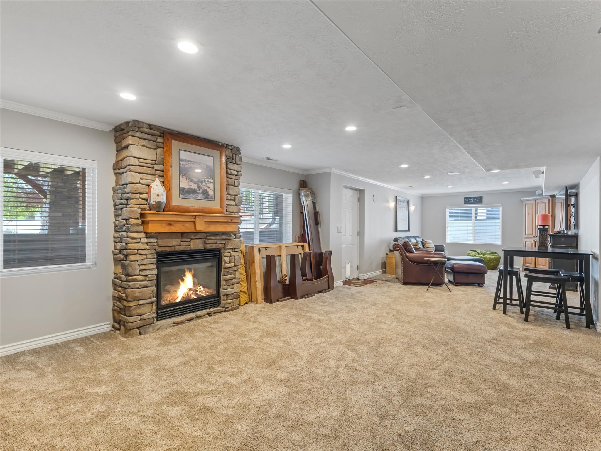Expansive carpeted basement area featuring a stone-clad fireplace with a wood mantle and a walk-out door to the backyard