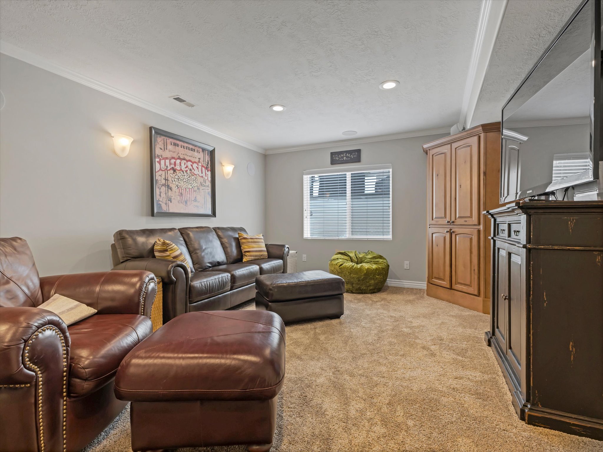 Basement carpeted entertainment area featuring recessed lighting, a window with blinds, and white crown molding