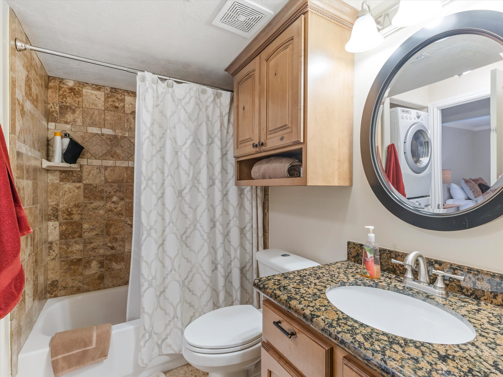 Basement bathroom vanity featuring a granite countertop with an undermount sink, brushed nickel faucet, and a large round mirror