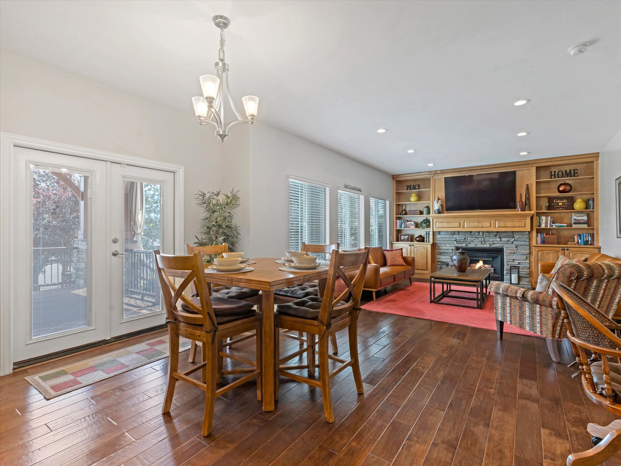 Open-concept living area featuring rich wood-finish flooring, a stone-faced fireplace with wood mantel, and built-in shelving