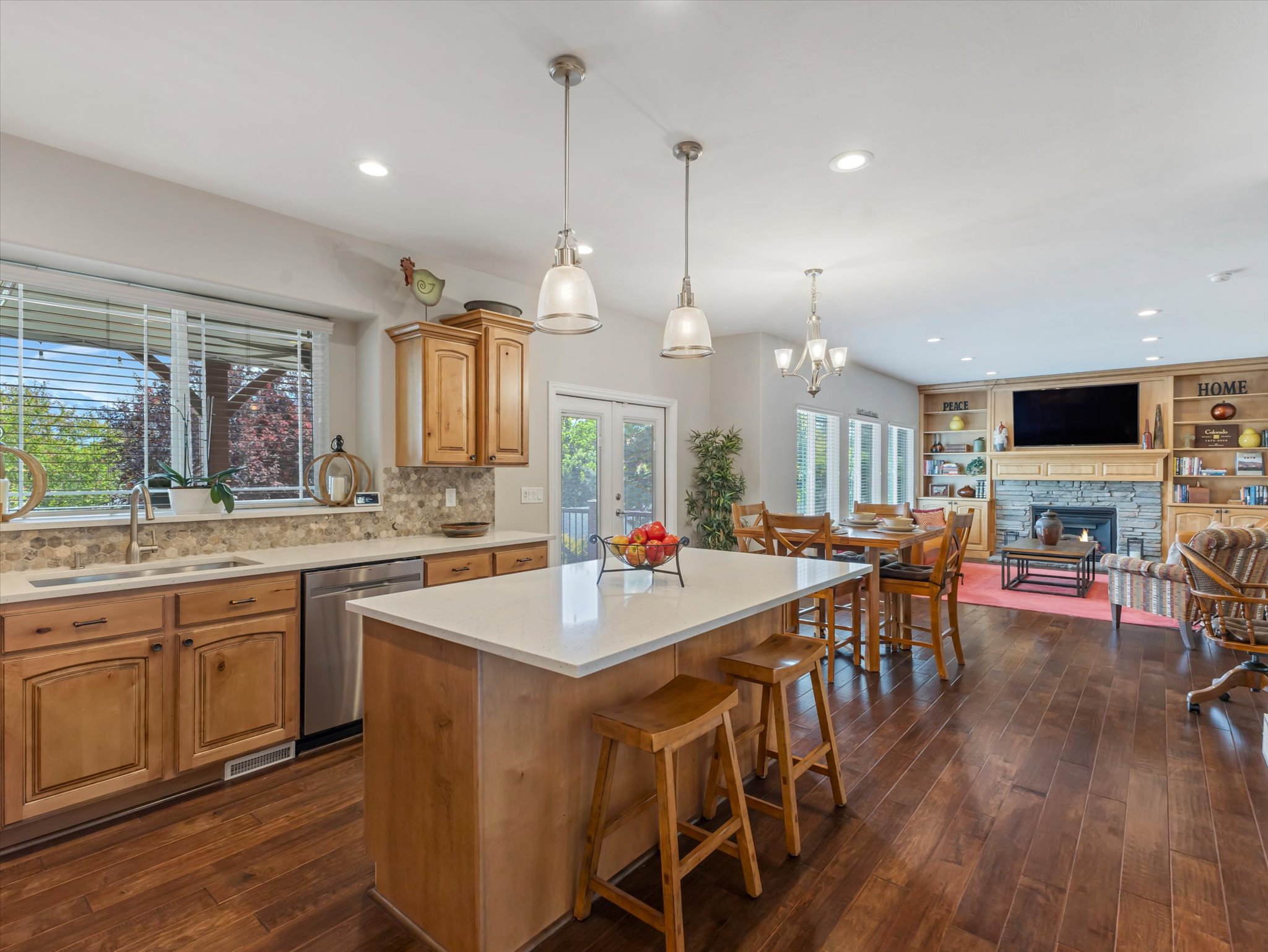 Open-concept living area featuring wood-finish flooring, a kitchen island with seating, stainless steel appliances, and a stone-faced fireplace with built-in shelving