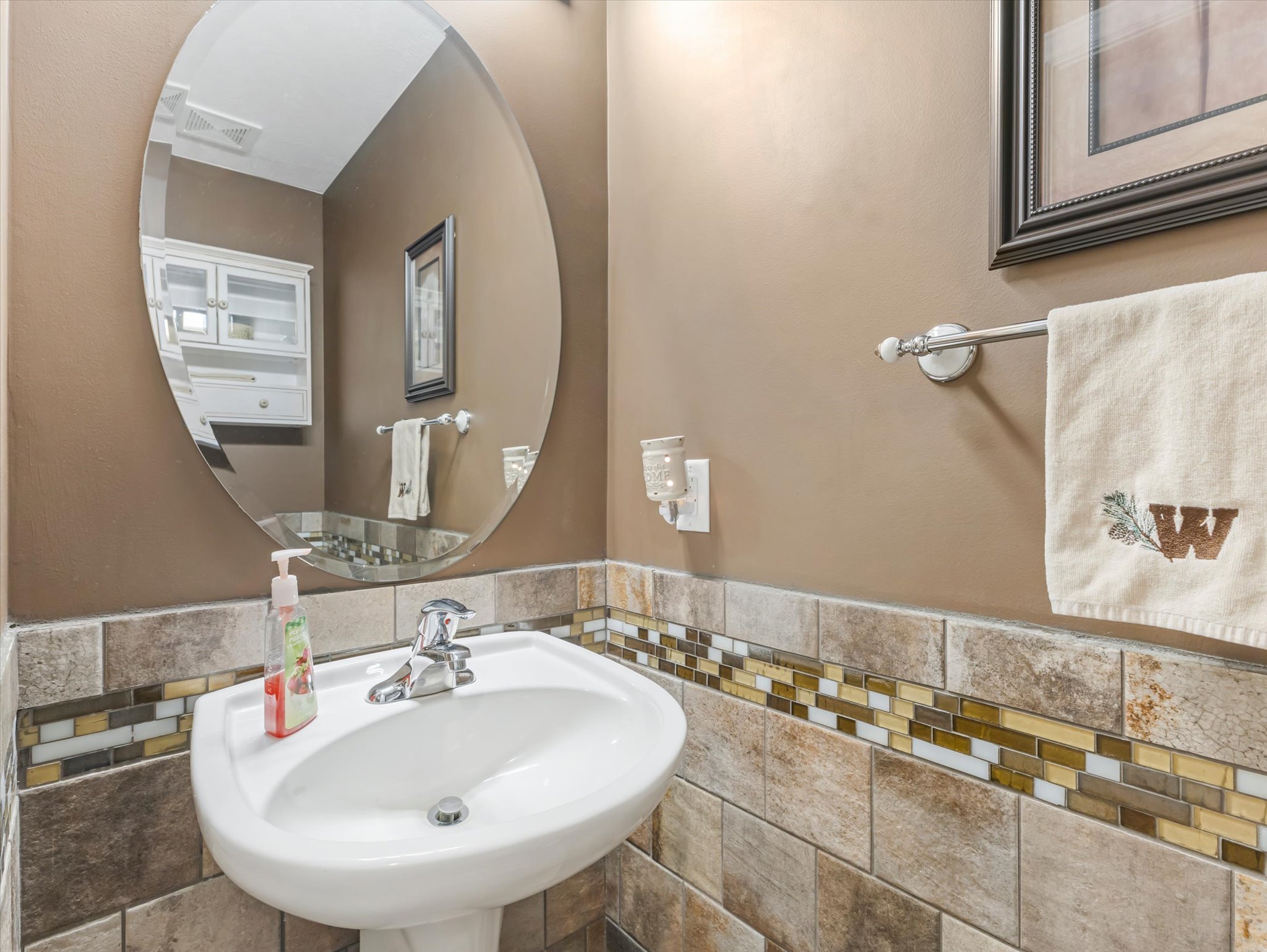 Main floor half bath with pedestal sink with chrome faucet set against a tiled wall