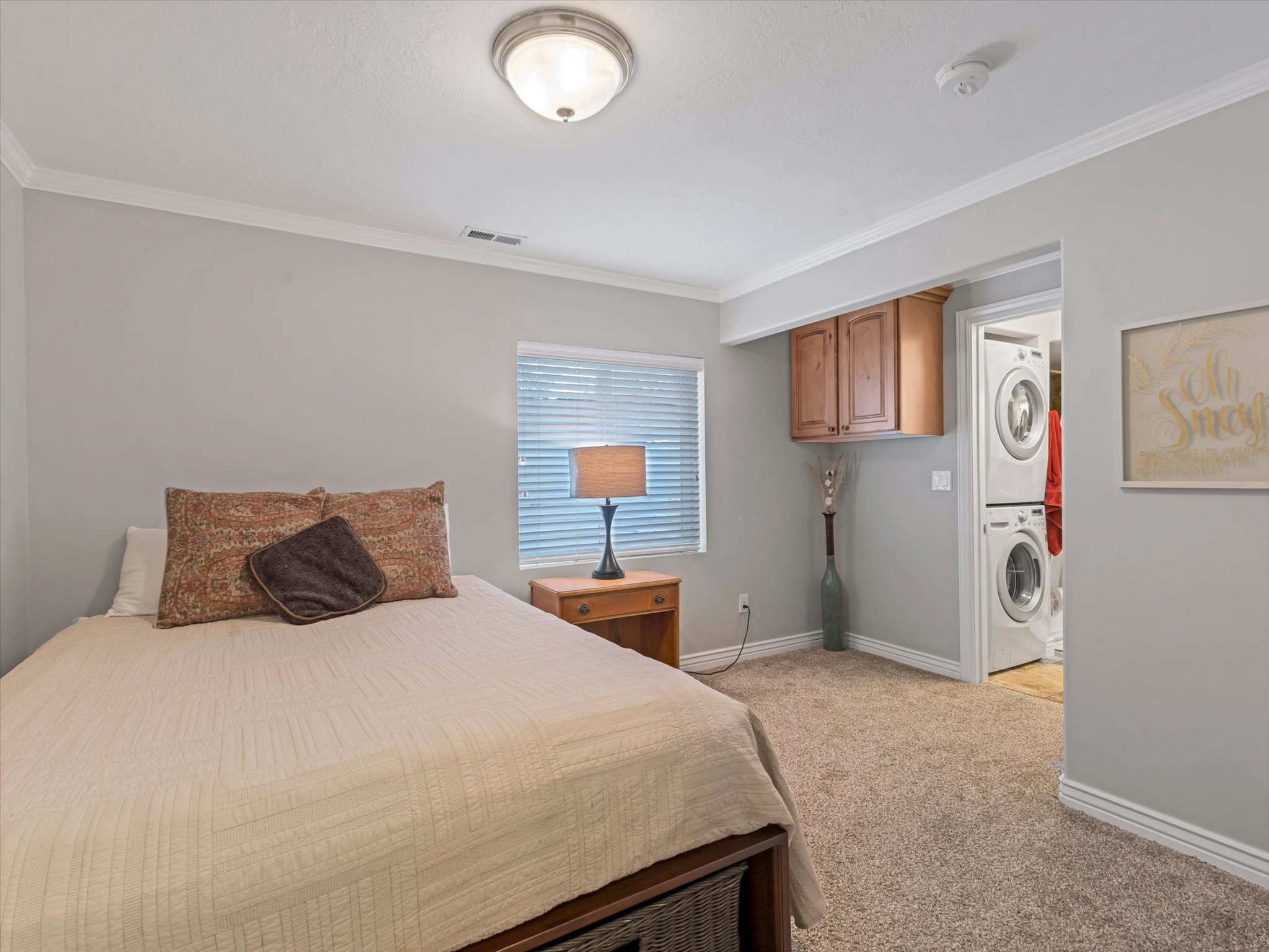Basement bedroom with carpet, with a window, crown molding, and a built-in laundry area featuring stacked appliances and wood cabinetry