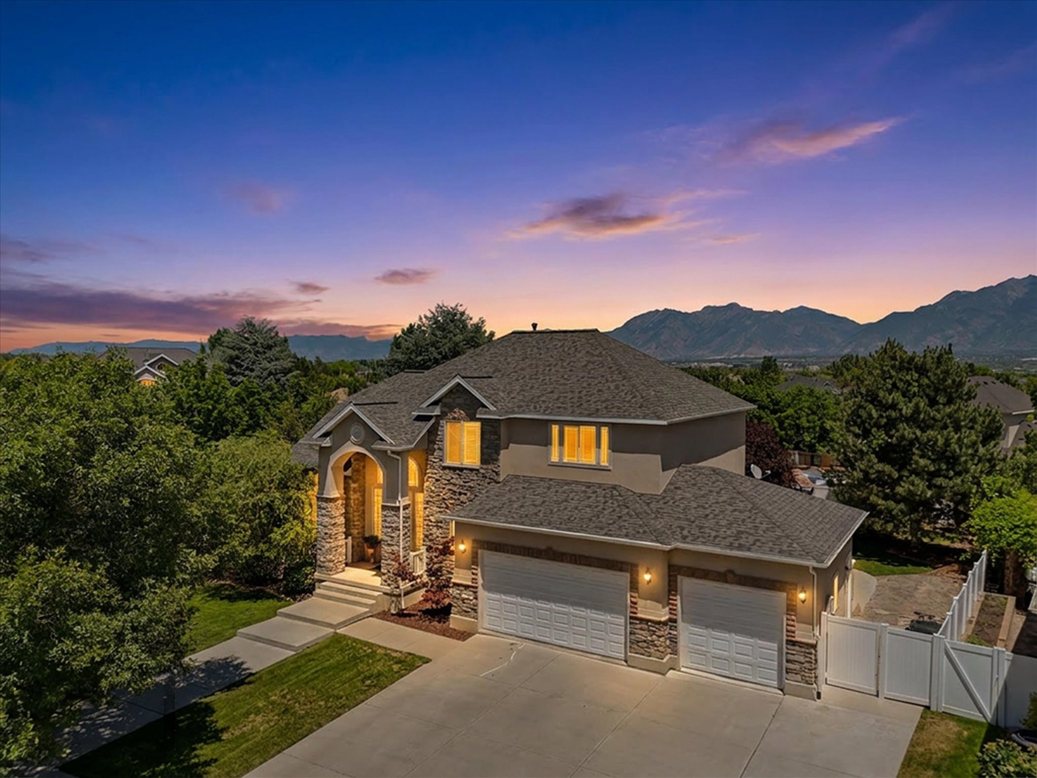 Front of residence featuring a stone and stucco exterior, a three-car garage, mature landscaping, and an arched entry with stone columns