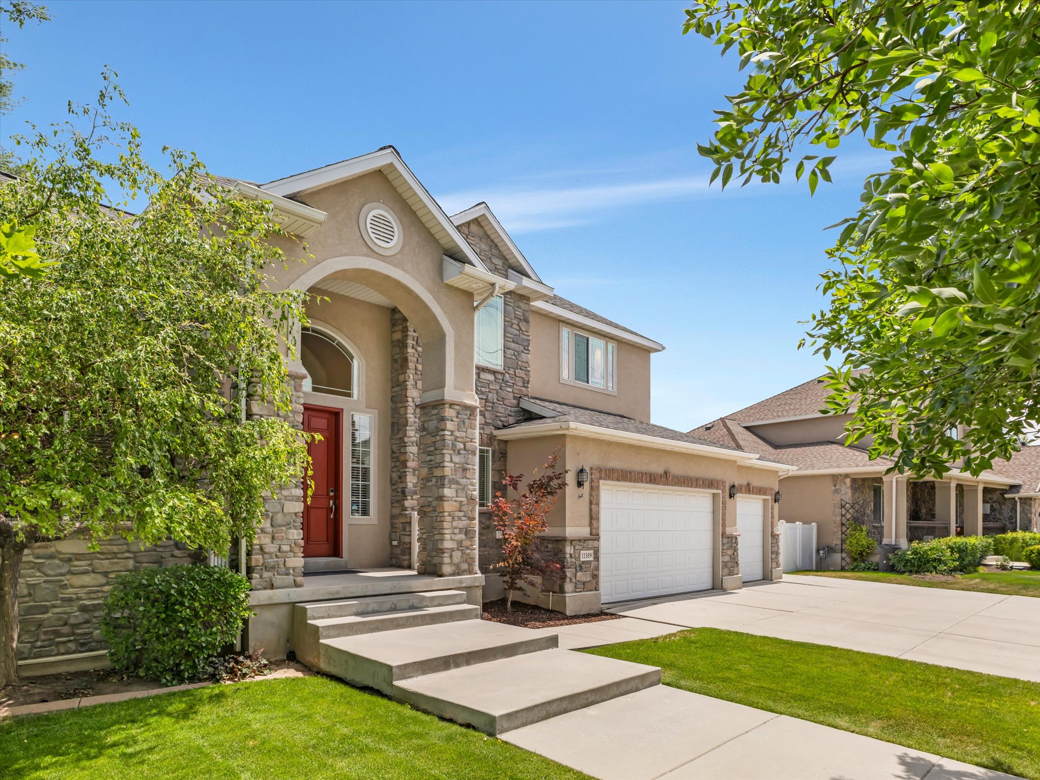 Two-story residence featuring a stone and stucco exterior, an arched entryway with a red door, a three-car garage, and a concrete driveway