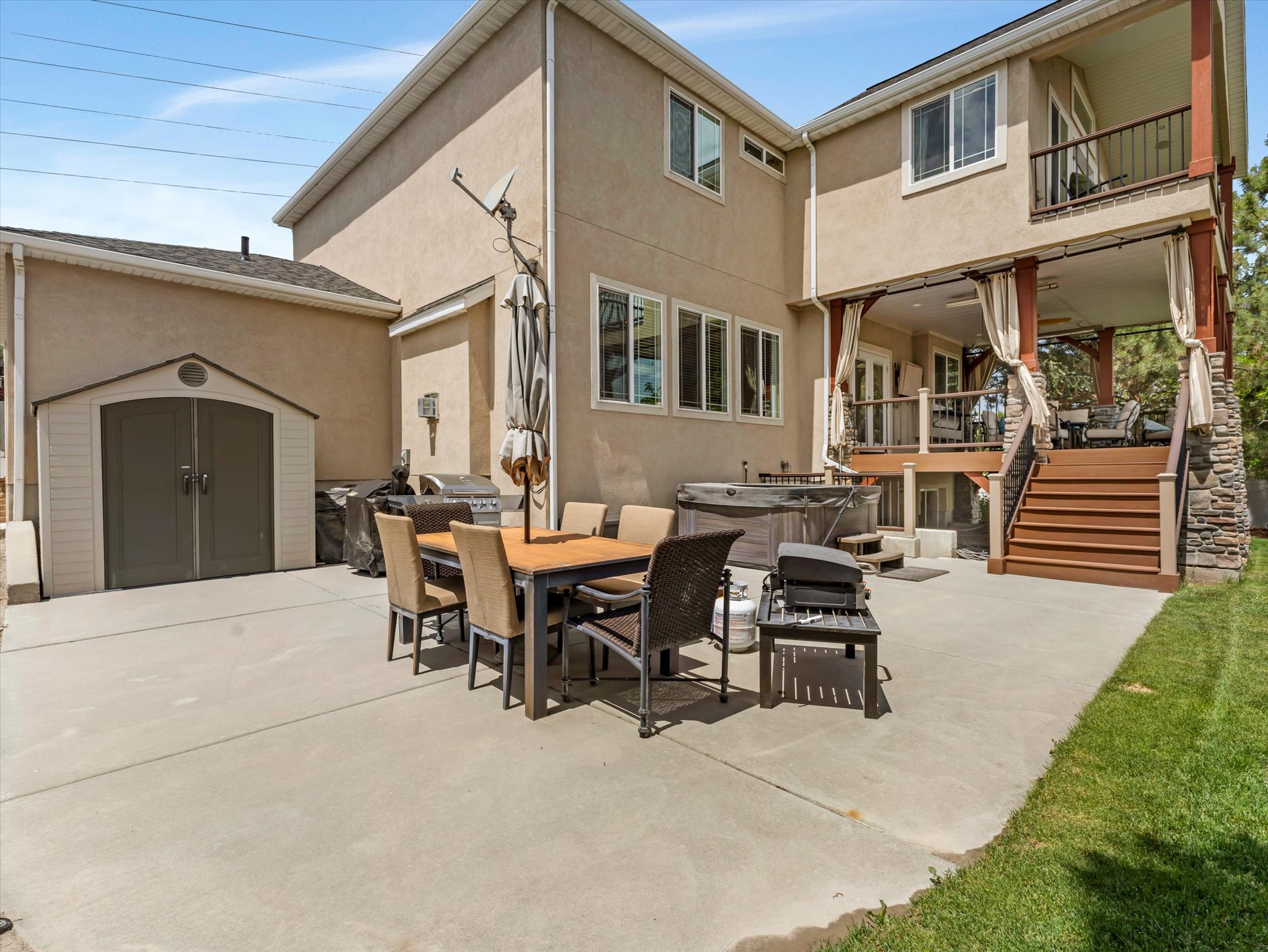 Expansive concrete patio featuring a dining area, hot tub, and exterior storage shed