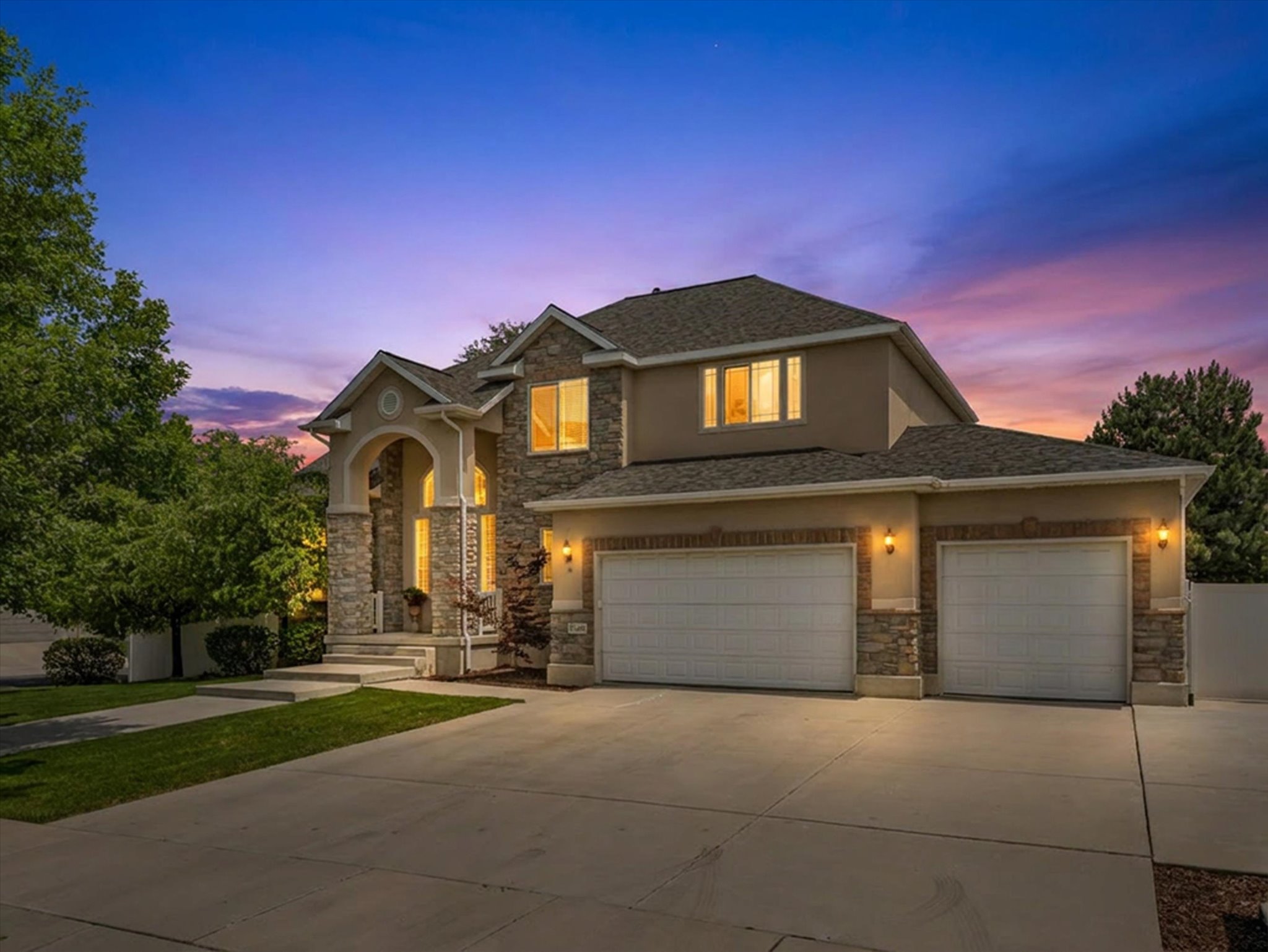 Stone and stucco exterior featuring a grand arched entry, multiple windows, and a three-car garage with individual doors