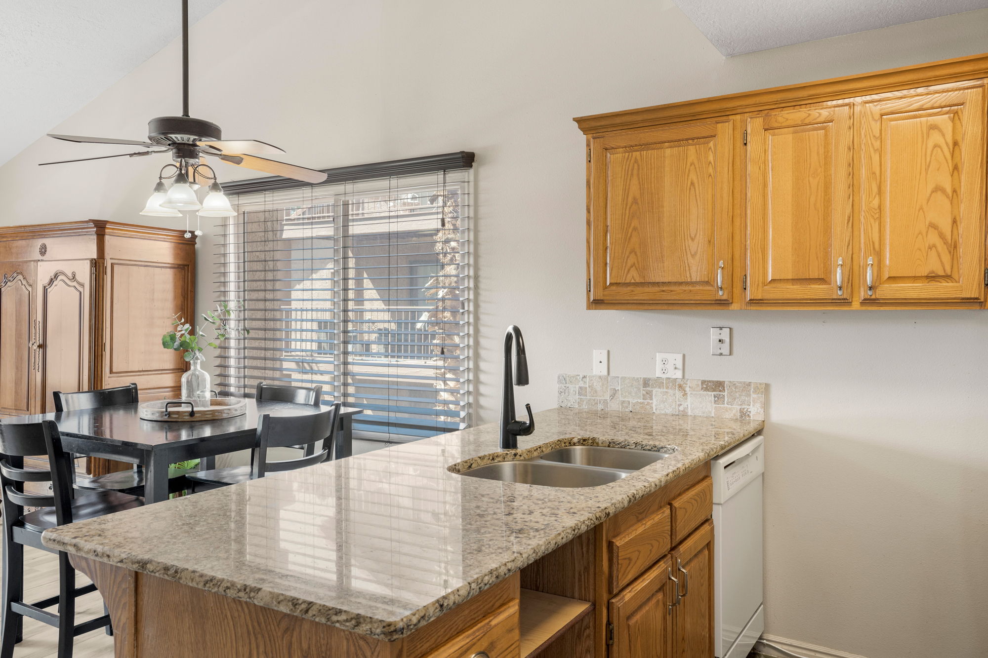 Kitchen island featuring a dual basin sink with a modern black faucet, granite-finish countertop, and integrated dishwasher