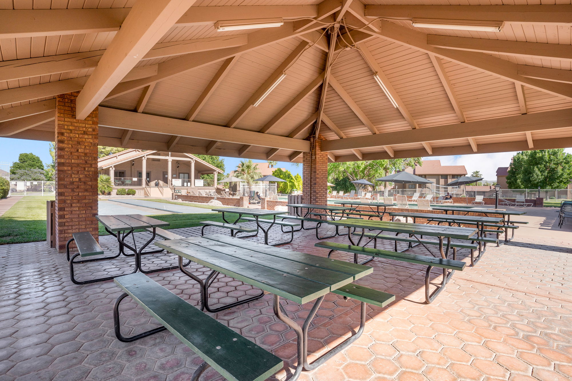 Covered outdoor patio area featuring multiple picnic tables with green-painted wood tops and black metal frames