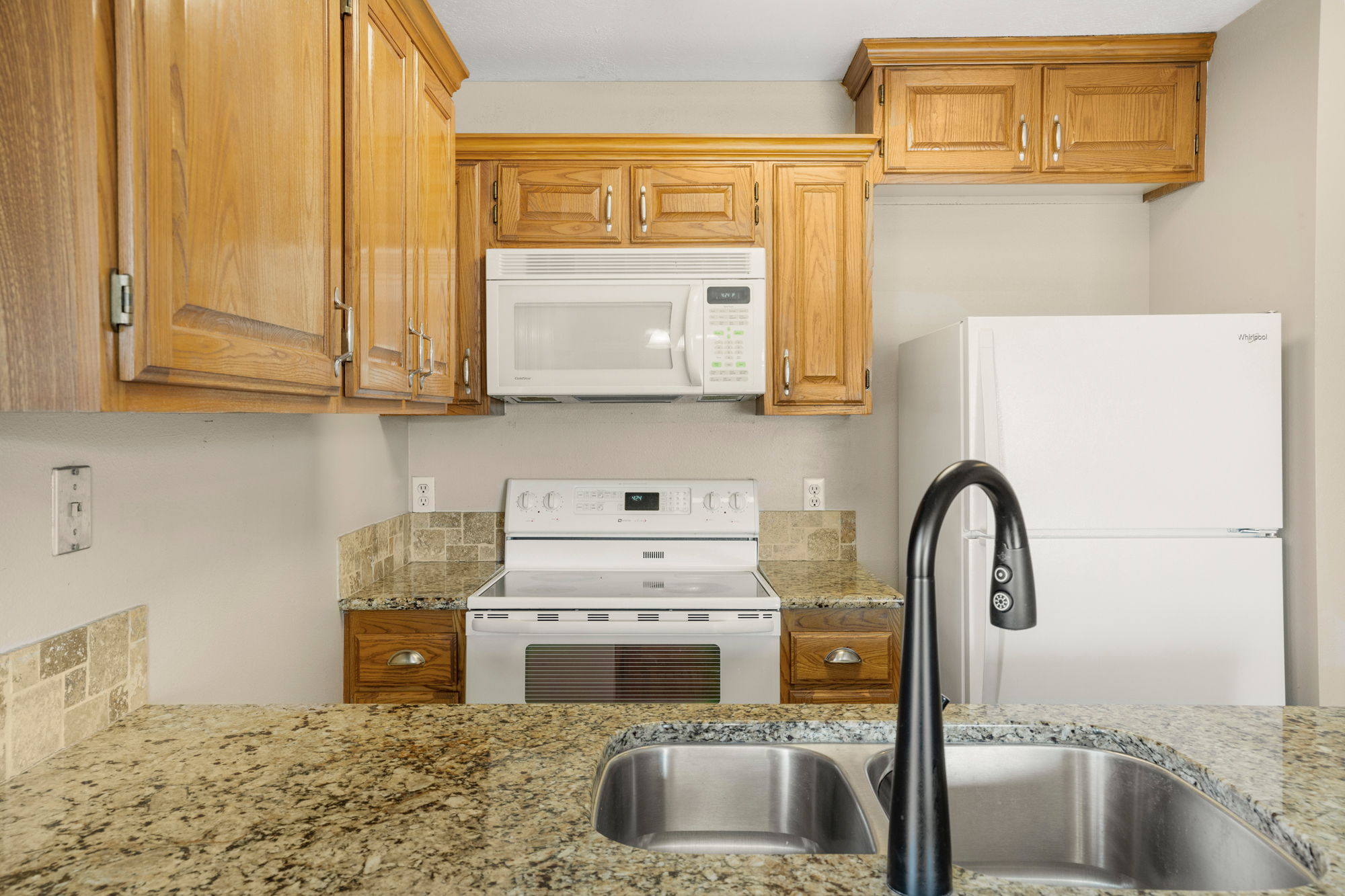 Kitchen featuring wood-finish cabinetry, speckled countertops, and a tiled backsplash