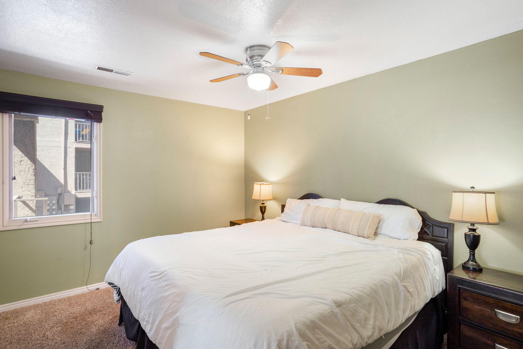 Bedroom featuring a ceiling fan with light fixture, neutral-toned walls, and a window with a dark roller shade