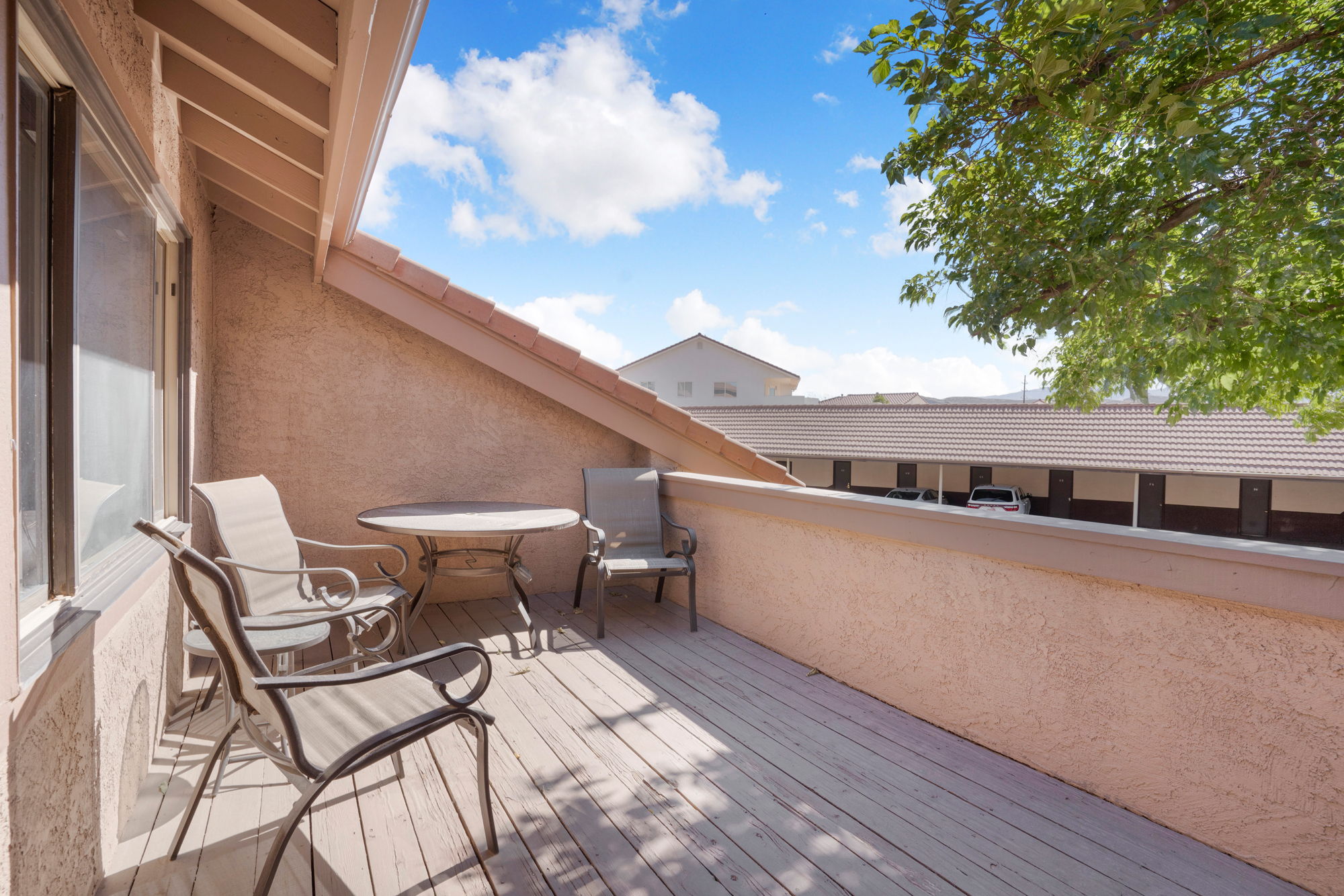Private balcony featuring wood-finish decking, stucco walls, and an angled roofline with tile accents