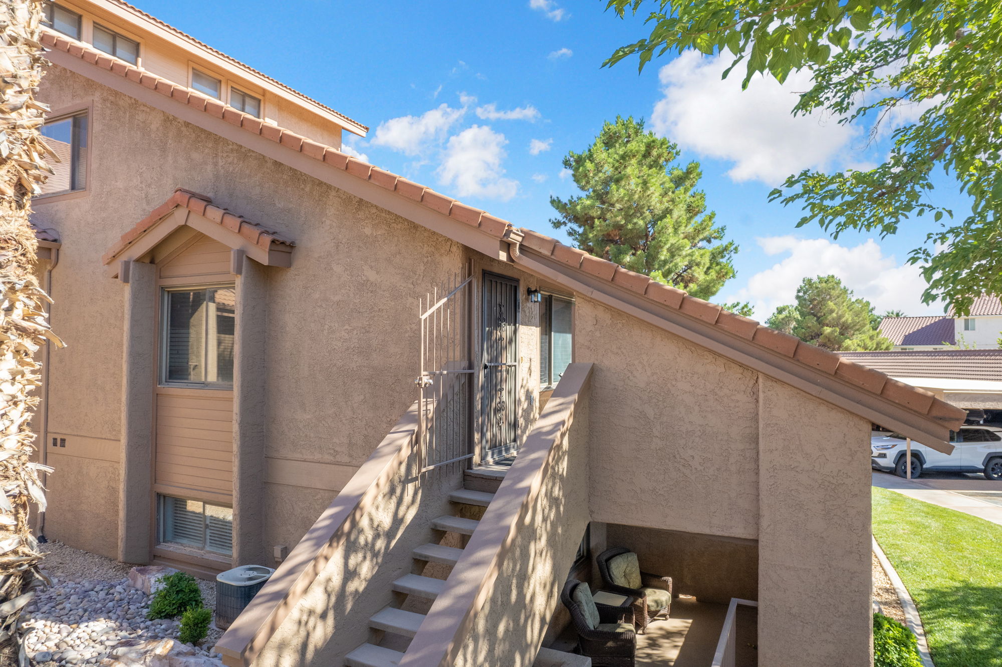 Multi-level stucco exterior with a tile roof, featuring an outdoor staircase, a shaded patio area, and mature landscaping