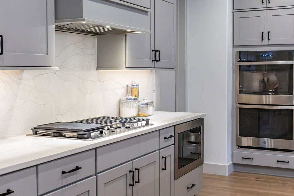 Modern kitchen featuring light gray cabinetry with matte black hardware, white countertops, a built-in gas cooktop, a stainless steel range hood, and a built-in double oven