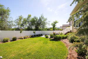 Expansive backyard featuring a manicured lawn, a white privacy fence, mature trees, a multi-level deck with white railings, and integrated landscaping